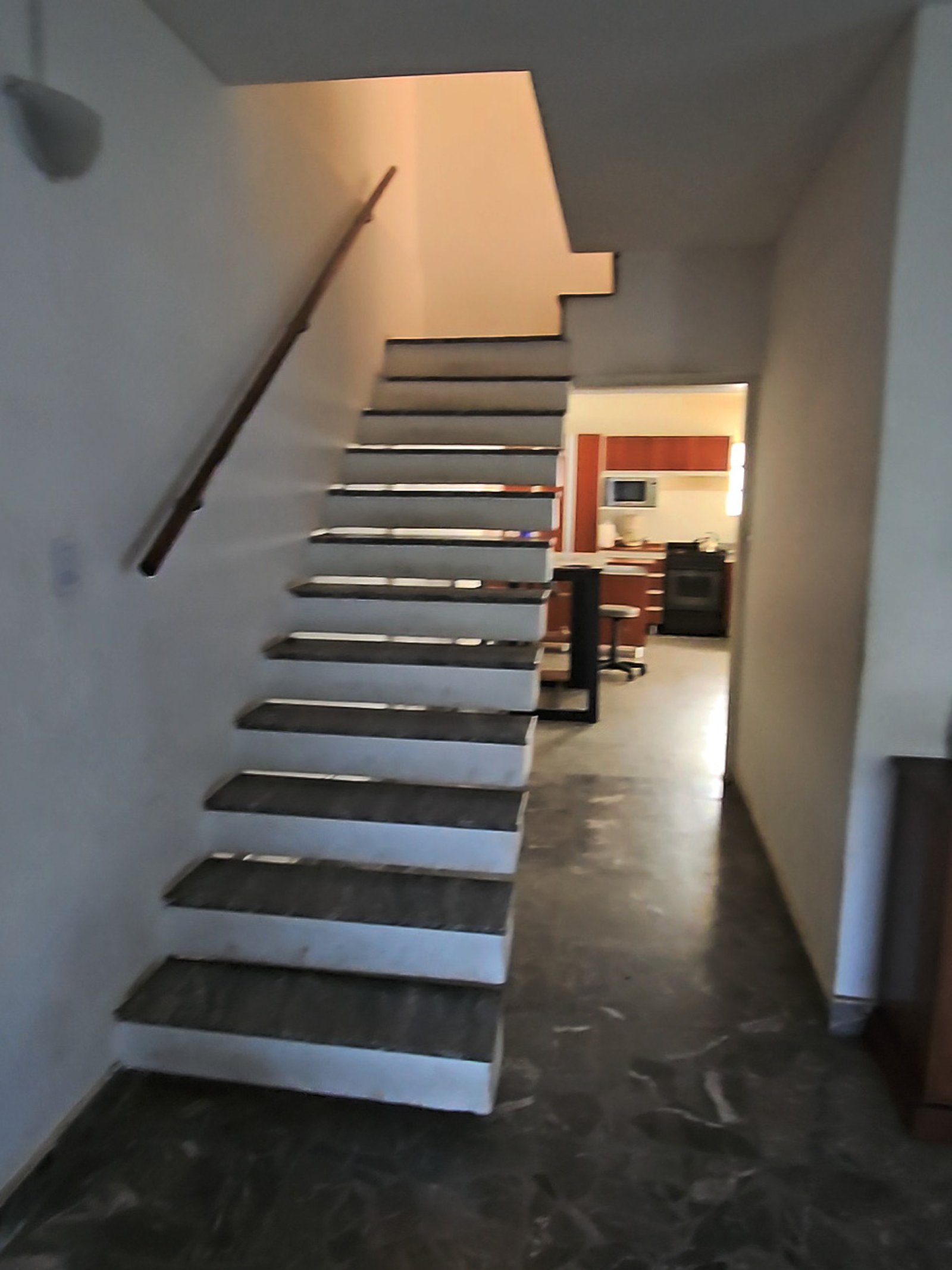 Escada flutuante moderna com piso de mármore e cozinha ao fundo — projeto Ballester, por BK Arquitectos, em B1653 Villa Ballester