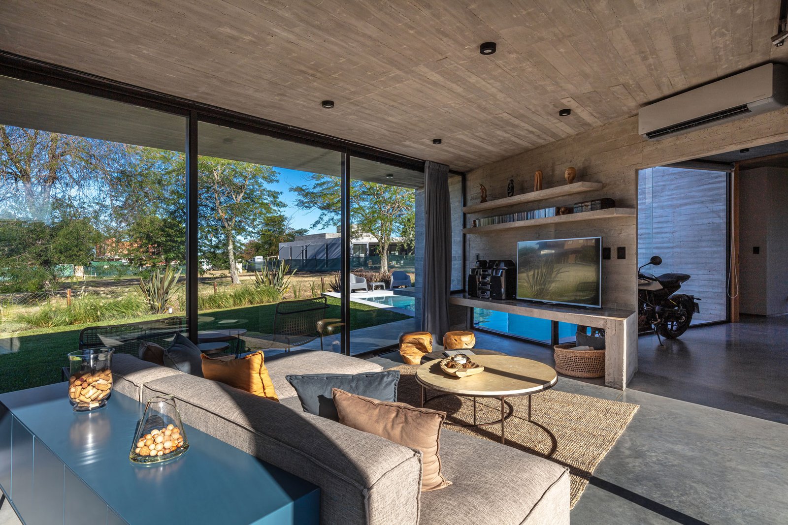 Living moderno con hormigón visto y ventanales al campo — proyecto Casa Pau, por Besonías Almeida arquitectos, en Guillermo Enrique Hudson