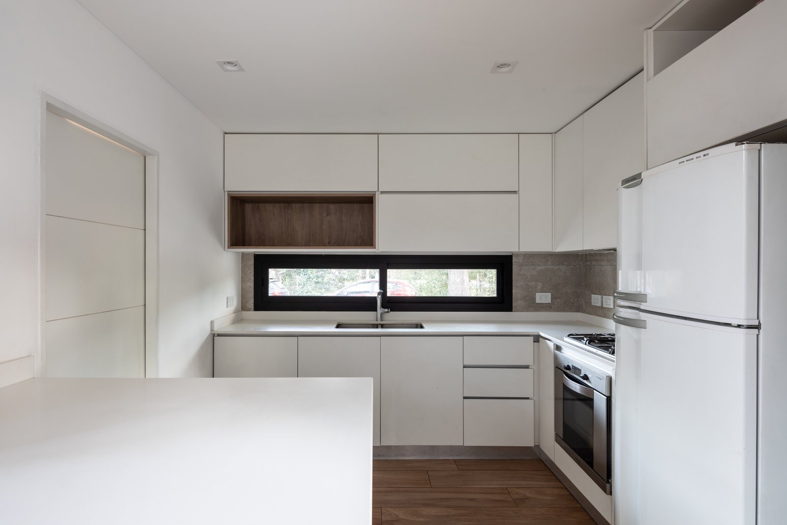 Cozinha moderna minimalista com armários brancos, bancada de microcimento e muita luz — projeto Casa Emilia, por Grupo CRBN, em Parque Leloir