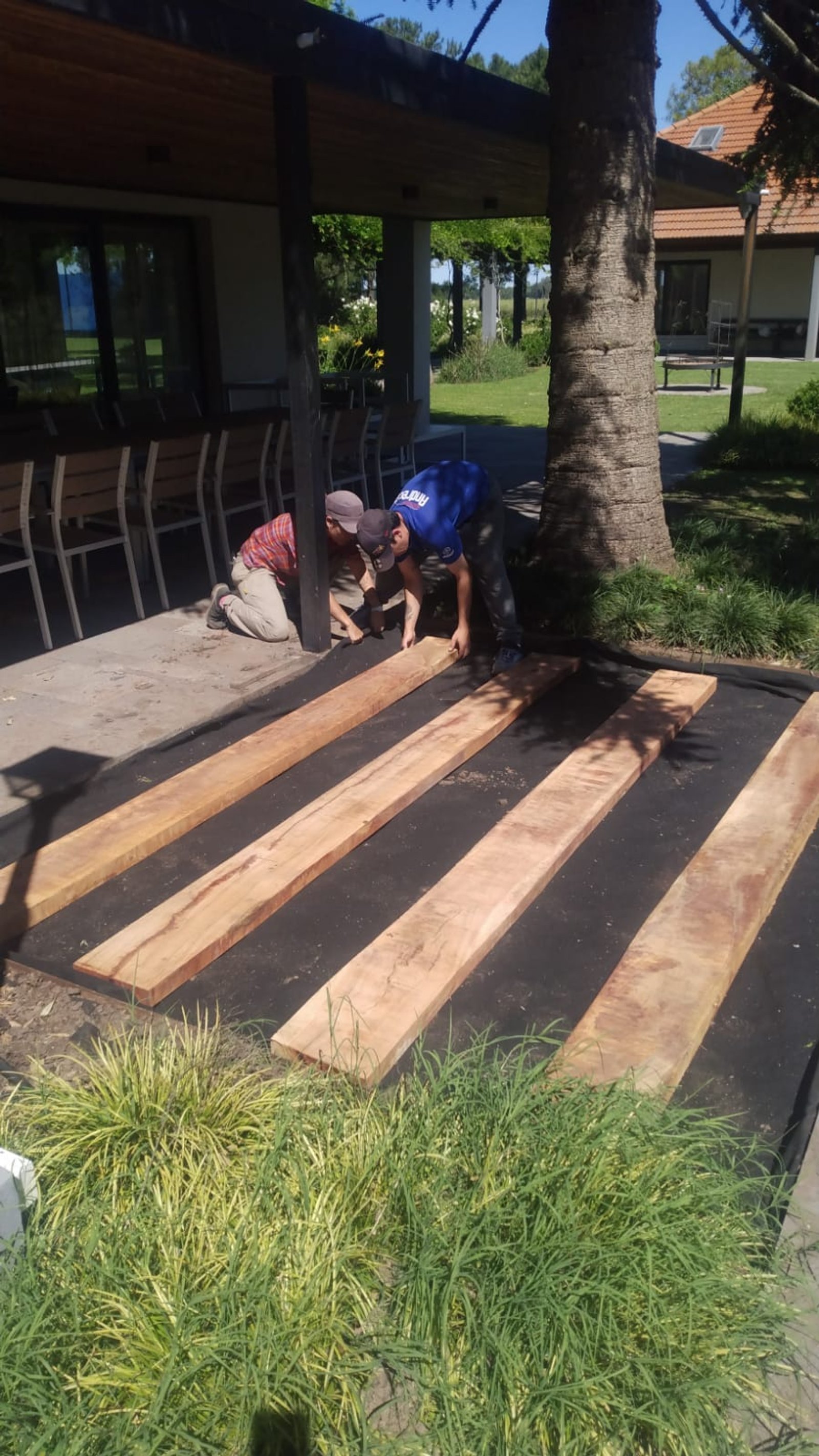 Colocación de tablones de madera en patio exterior con operarios — proyecto Casa COAL, por Estudio Rifahi, en B2814 Los Cardales