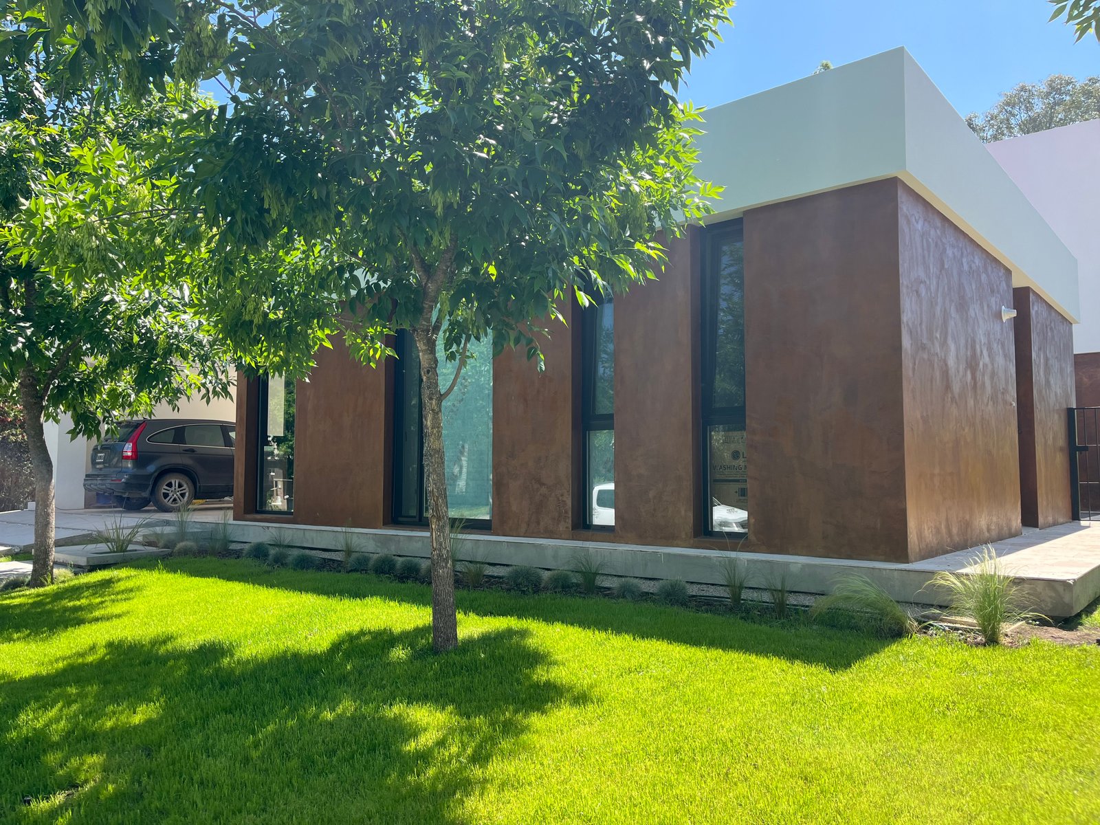 fachada moderna con revestimiento oscuro y césped — proyecto Casa La Reserva , por Marianela Grosso, en Ruta Panamericana No. 9 Km 61