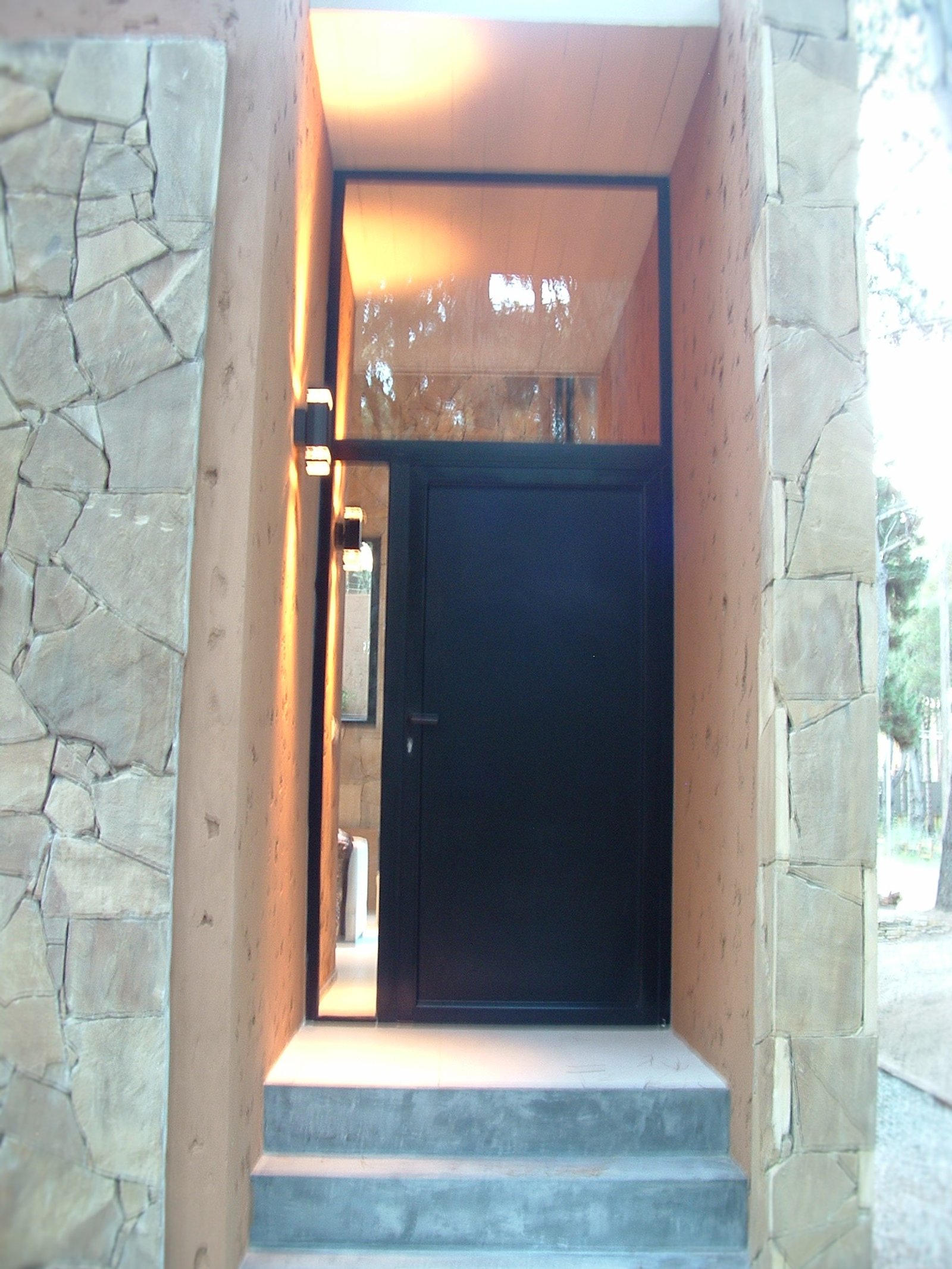 Entrada moderna con puerta negra y pared de piedra texturizada — proyecto LA  ALHAMBRA, por GJF estudio, en Costa del Este