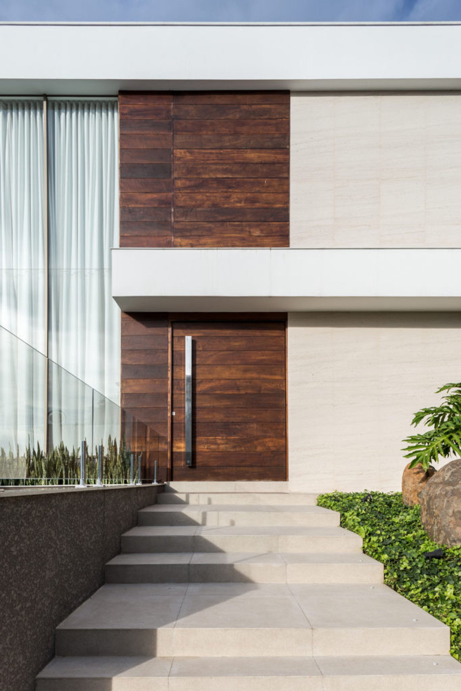 Fachada moderna com painéis de madeira, pedra e janelões com escada de azulejos — projeto Casa MC, por Boscardin Corsi Arquitetura