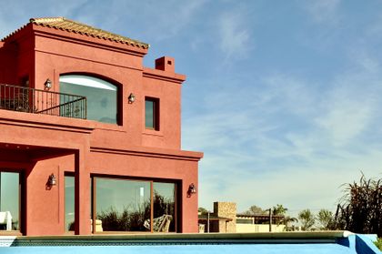Casa terracota con pileta y cielo azul en un día soleado — proyecto San Marcos 2, por Marconi Silva Arquitectos, en Benavidez