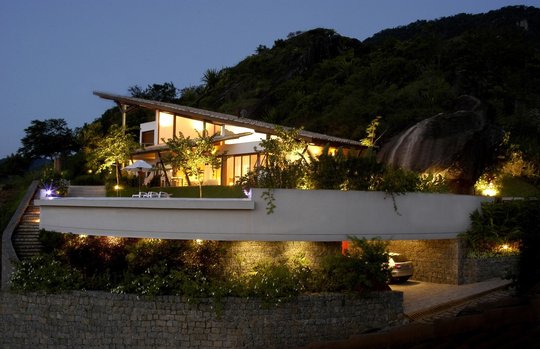 Casa moderna en ladera con fachada blanca iluminada al atardecer — proyecto Residência TE, por Gil Fialho