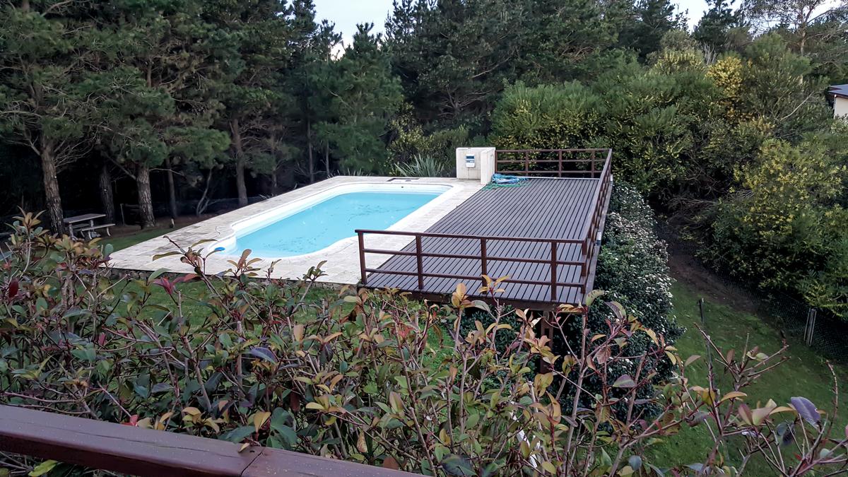 piscina moderna com deck de madeira e vegetação exuberante — projeto Vivienda Unifamiliar en Costa Esmeralda, por Estudio Schifano, em Costa Esmeralda