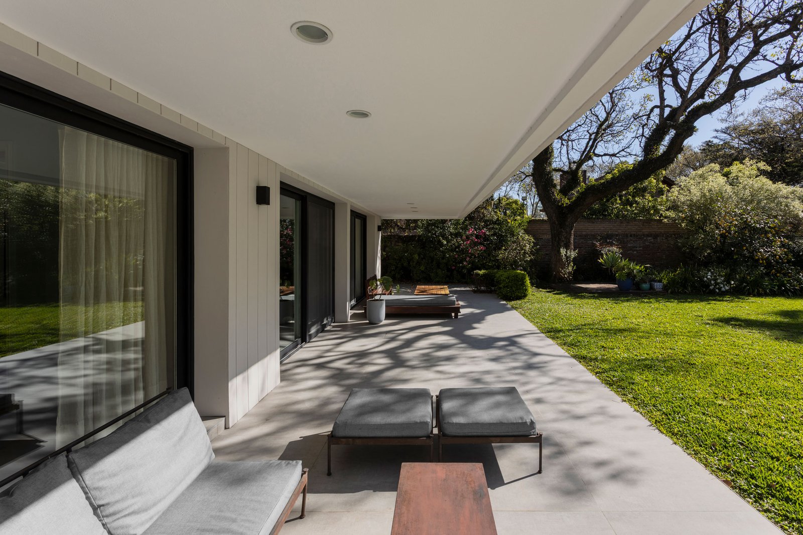 Patio moderno con gran alero, césped exuberante y mobiliario gris — proyecto REFORMA DG, por Rastro Estudio, en Punta Chica