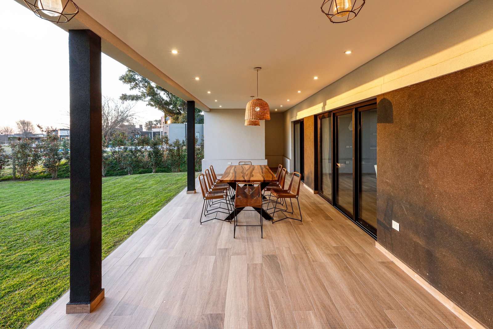 Comedor exterior sobre deck de madera con lámparas colgantes de ratán — proyecto SS45, por EZ architects, en Pilar