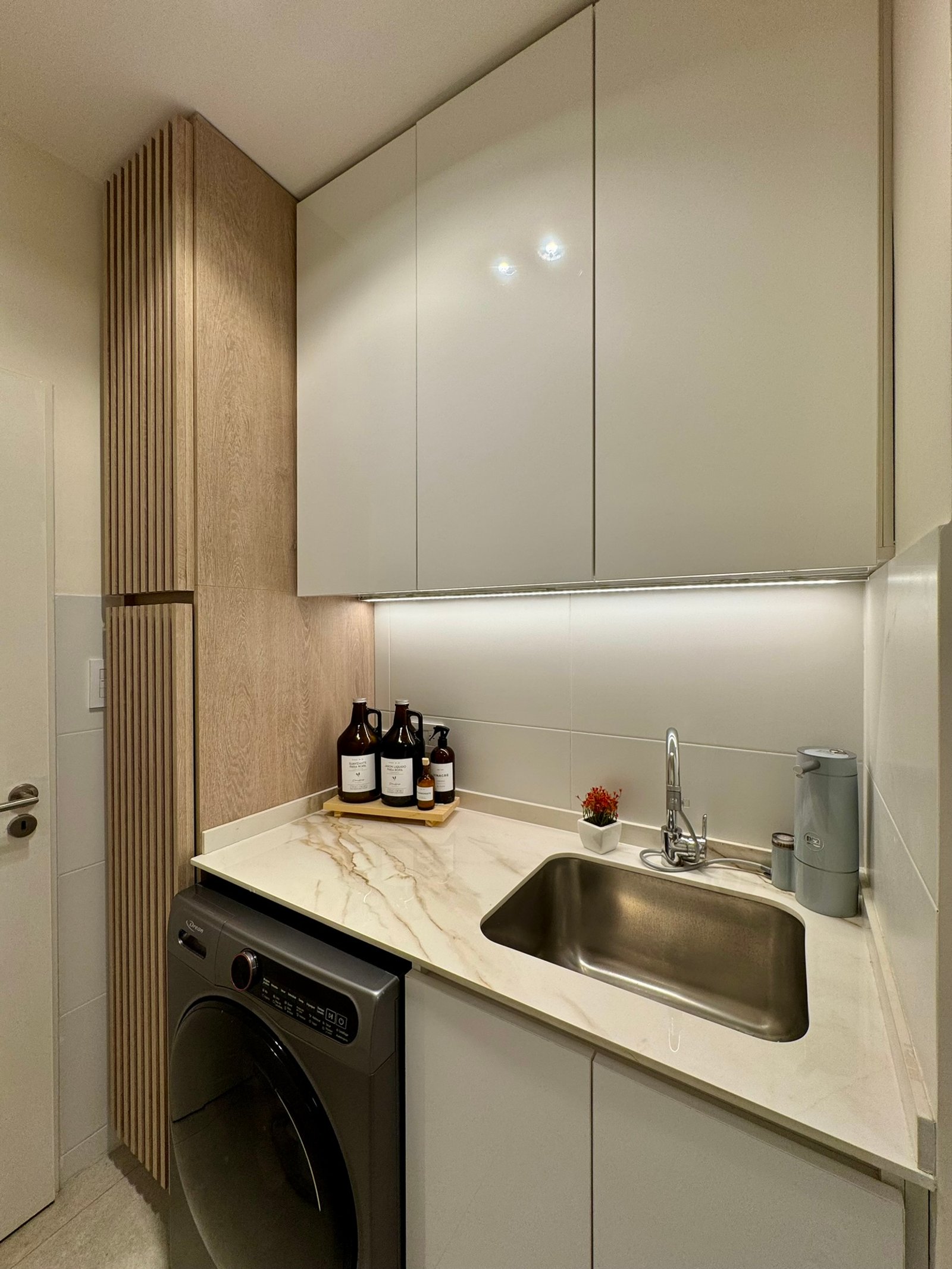 Lavadero moderno con gabinetes blancos, madera veteada y mesada símil mármol — proyecto Corrientes I, por MDBK Arquitectura, en Villa Crespo