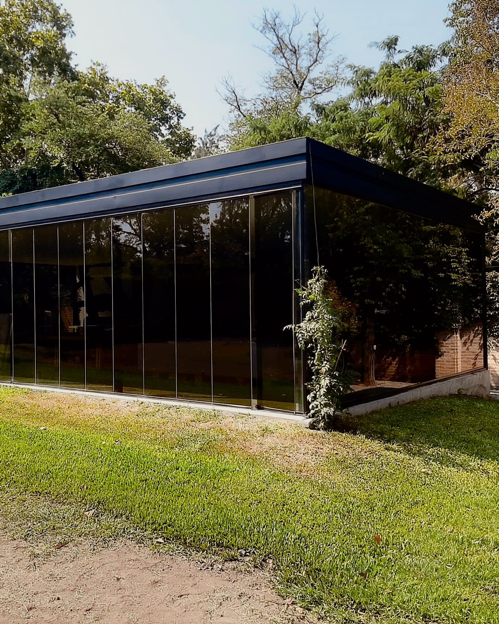 Estructura moderna de cristal con ventanas de piso a techo en entorno boscoso — proyecto FILMS 3M de control Solar, Seguridad y Privacidad, por Grupo Laminar 