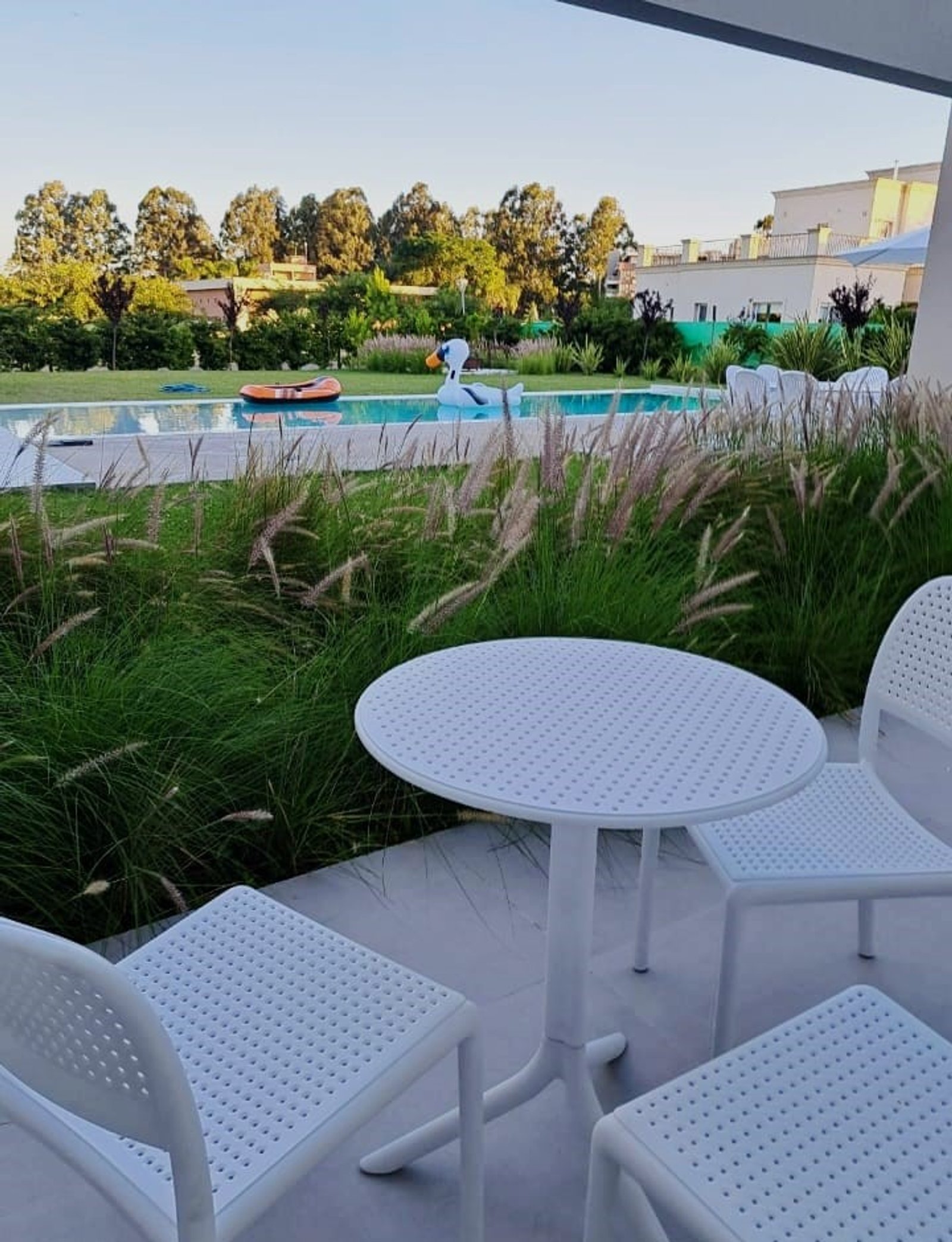 Muebles blancos perforados junto a la piscina rodeados de vegetación alta — proyecto Balcón y Terraza, por Casa Nuñez