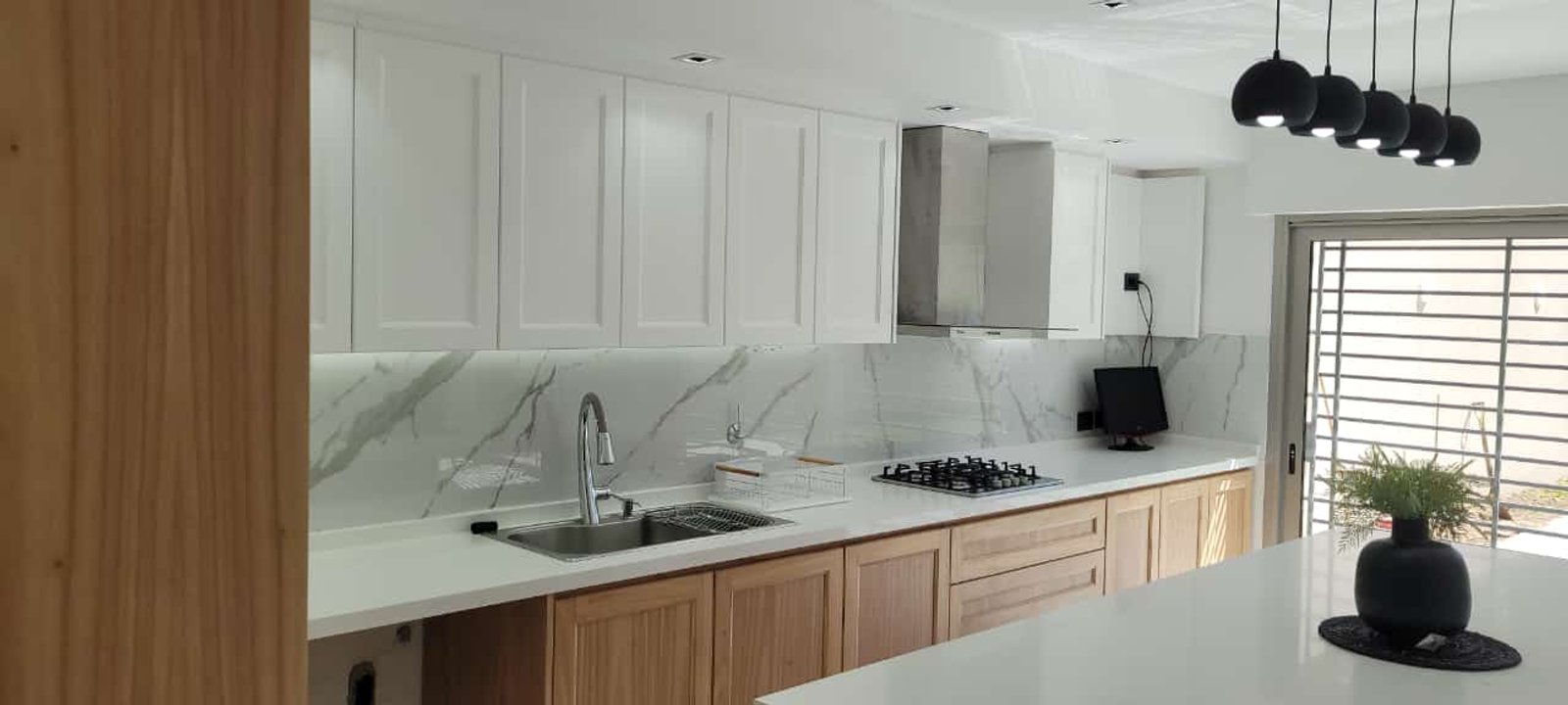 Cocina moderna con isla, gabinetes de madera y blancos, y luces colgantes negras — proyecto Ramos, por Licefe Carpentry SRL, en B1704 Ramos Mejía