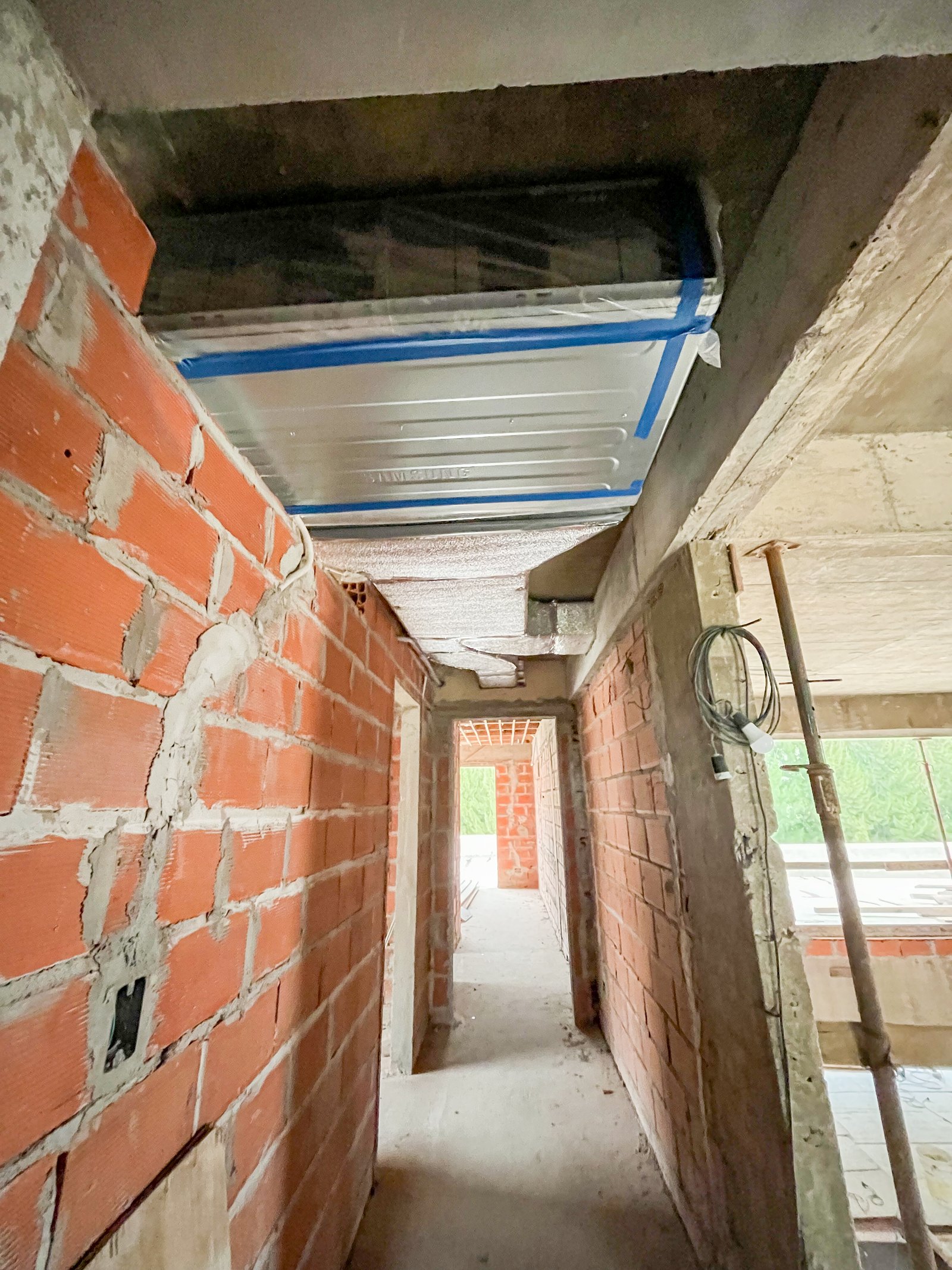Corredor em construção com paredes de tijolo e teto de concreto — projeto Obra VRV Terravista, por Climatizacion HD, em Av. Gaona