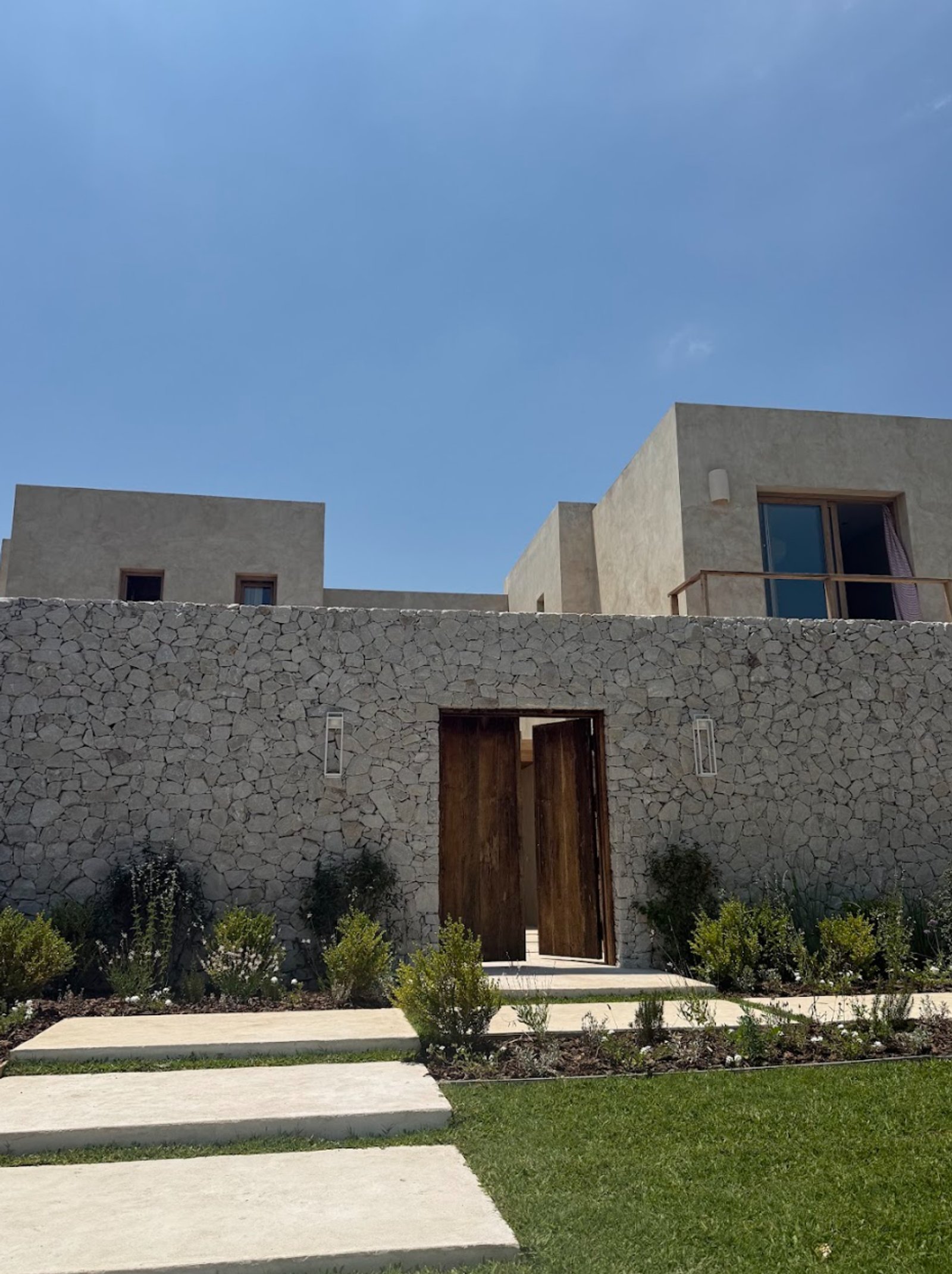 Fachada moderna con muro de piedra y puertas de madera rústica — proyecto La Verbena, por Grupo Pauta Arquitectura, en Alejandro Korn 3150