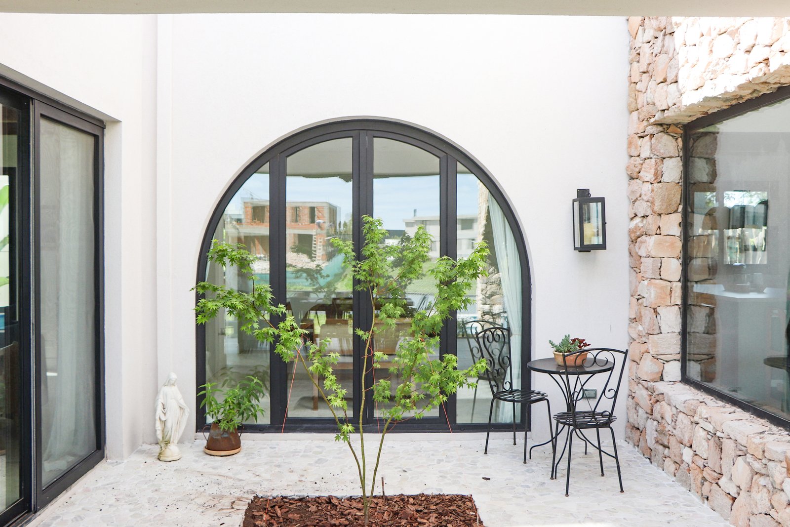 Patio mediterráneo con ventana arqueada de cristal y piedra — proyecto Casa San Fermin 62, por R+B arquitectos, en Pasteur 662