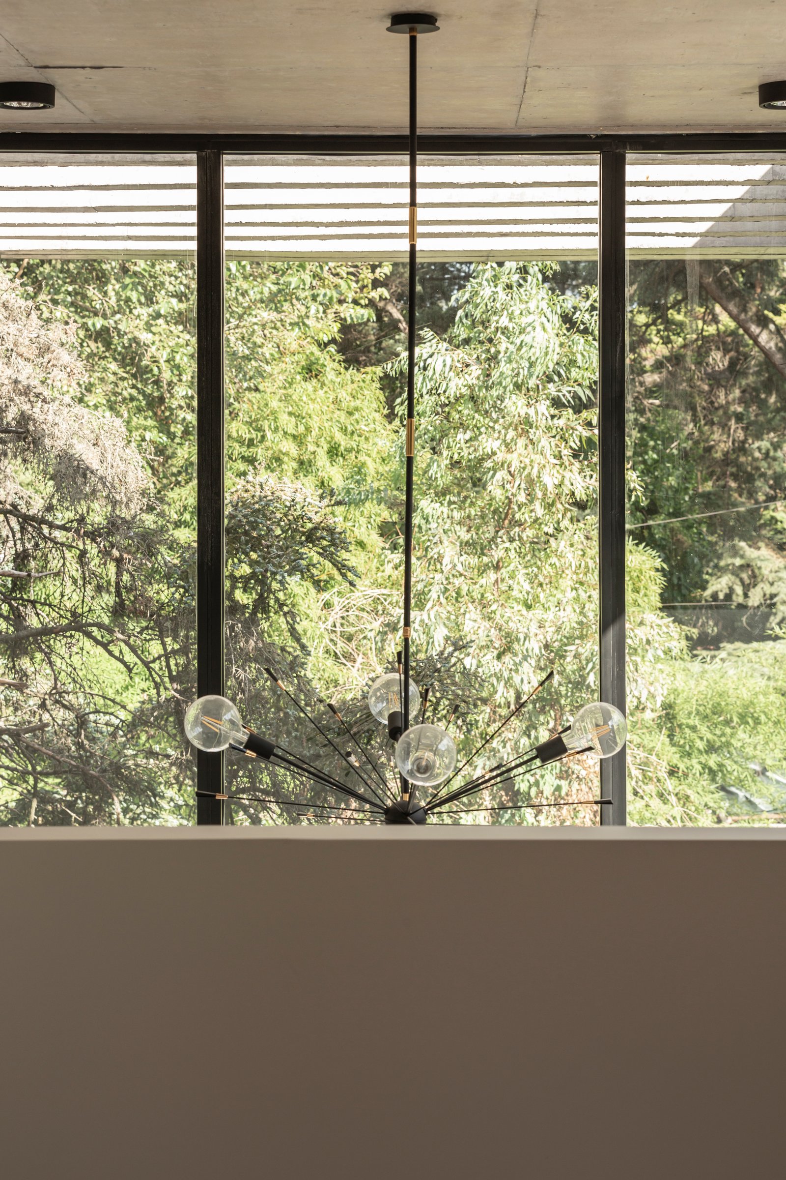 Living con araña moderna y ventanales al bosque — proyecto Casa Emilia, por Grupo CRBN, en Parque Leloir
