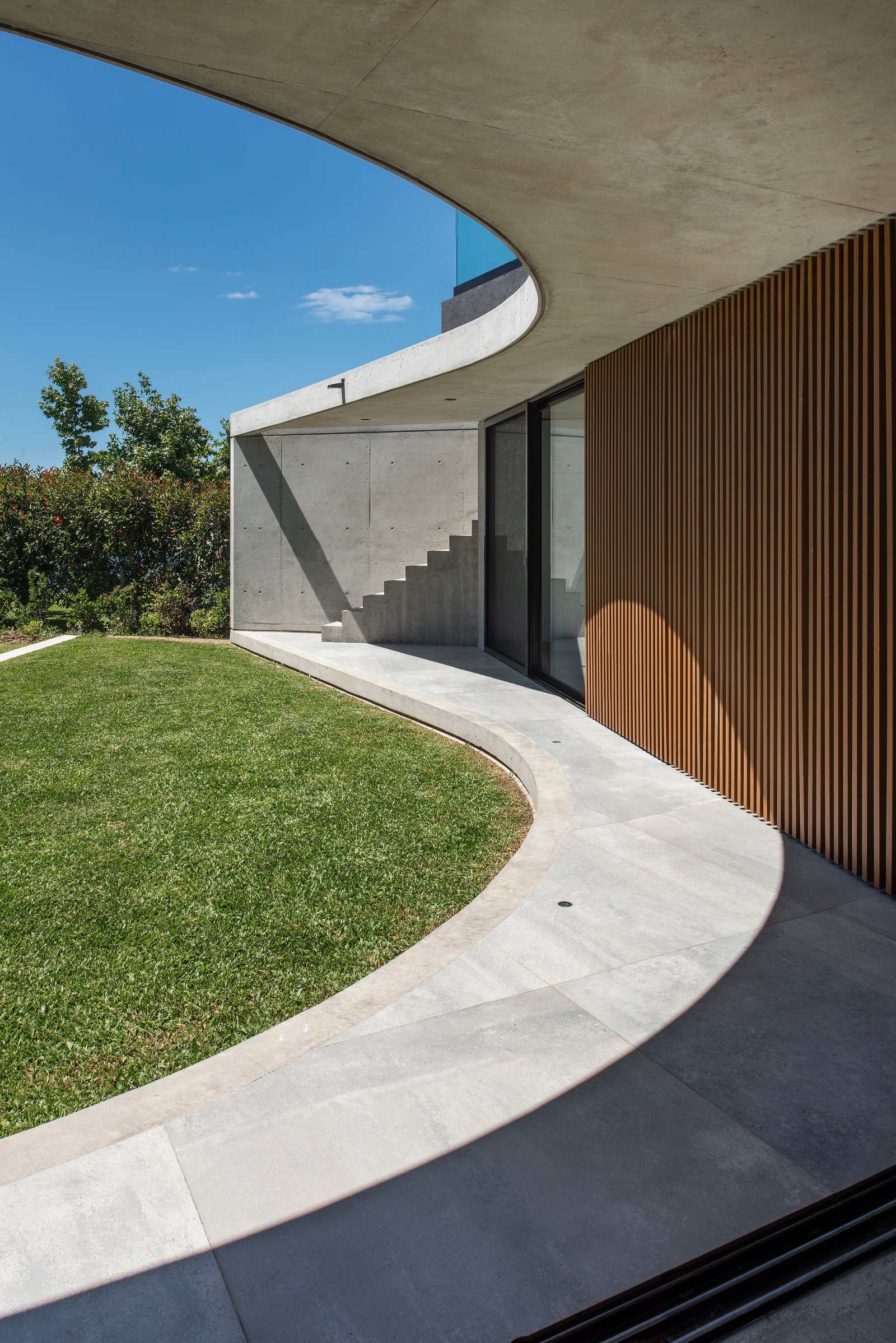 Fachada moderna curva con césped y escaleras integradas — proyecto Obra Muelles, por lifecycle, en Av. de los Lagos