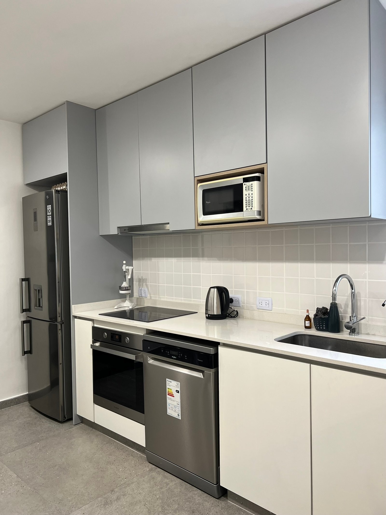 Cozinha moderna com armários cinza e branco, eletrodomésticos embutidos e bancada branca — projeto Vera I, por MDBK Arquitectura, em Villa Crespo