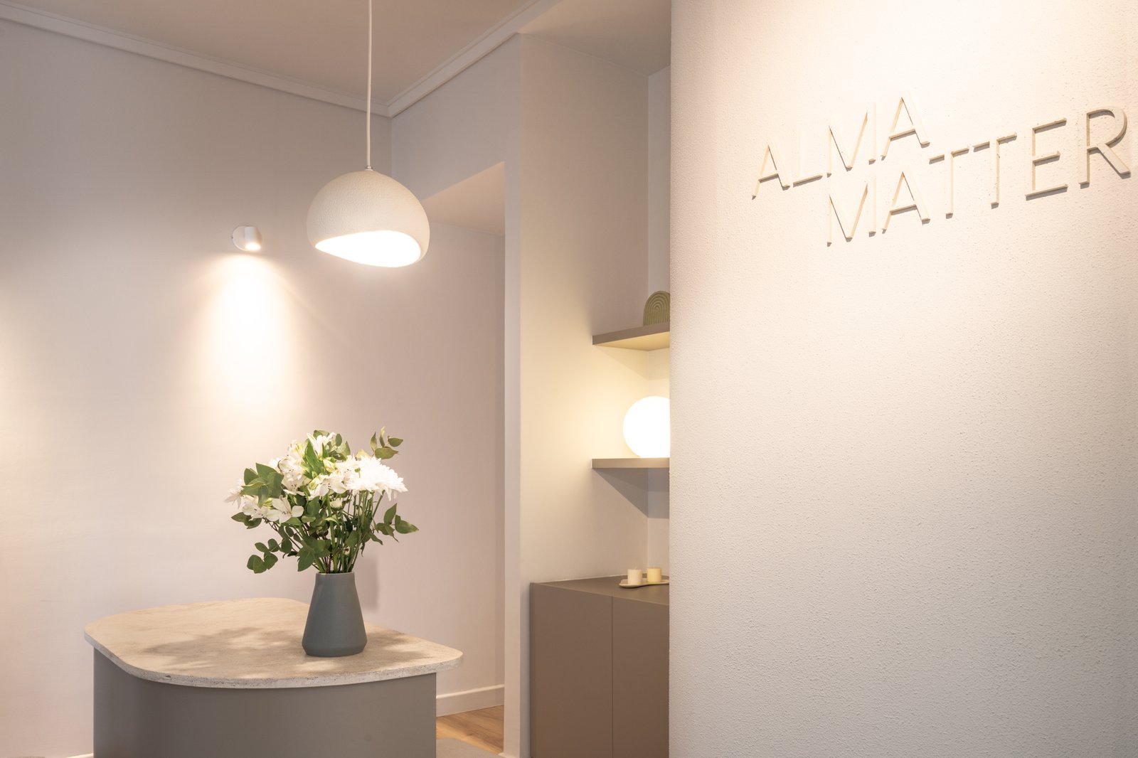 Espacio comercial minimalista con flores y luz cálida — proyecto ALMA MATTER, por Maria Menna Arquitecta, en Mar del Plata
