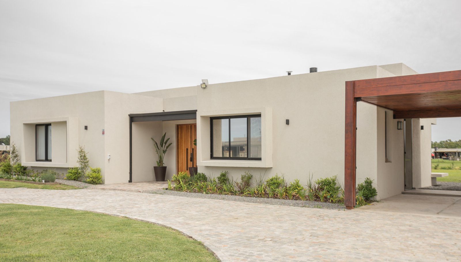Fachada moderna de casa unifamiliar con pérgola de madera — proyecto CASA AB, por SEDE Arq., en Av. Pereda S/N