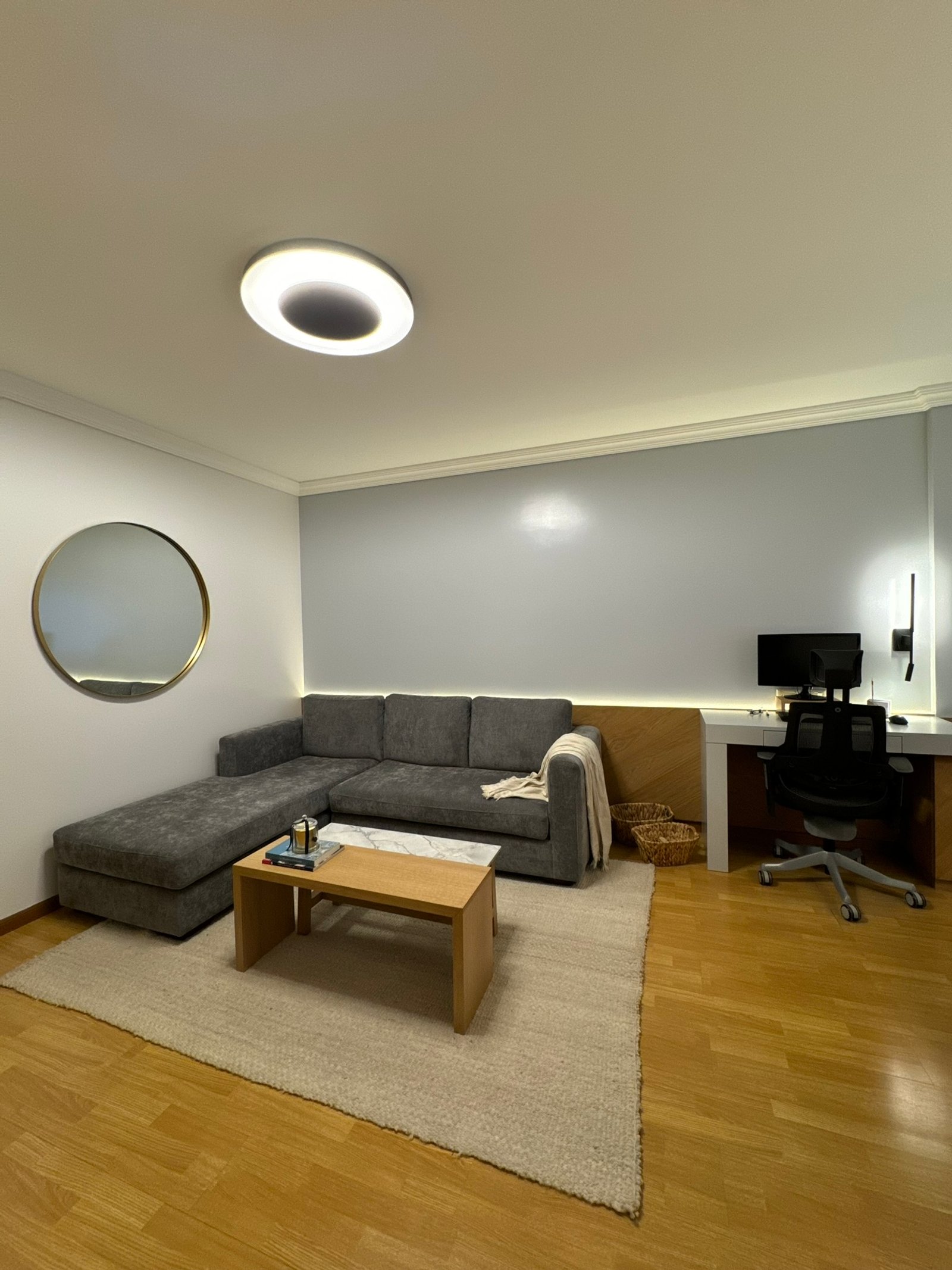 Sala de estar moderna con sofá seccional gris oscuro, alfombra beige y escritorio de oficina — proyecto Thompson, por MDBK Arquitectura, en Caballito
