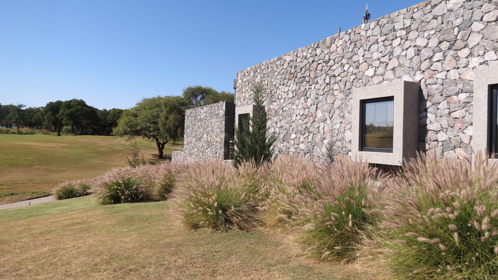 fachada moderna con piedra y pasto alto — proyecto El Terrón, por Estudio Rifahi, en Mendiolaza