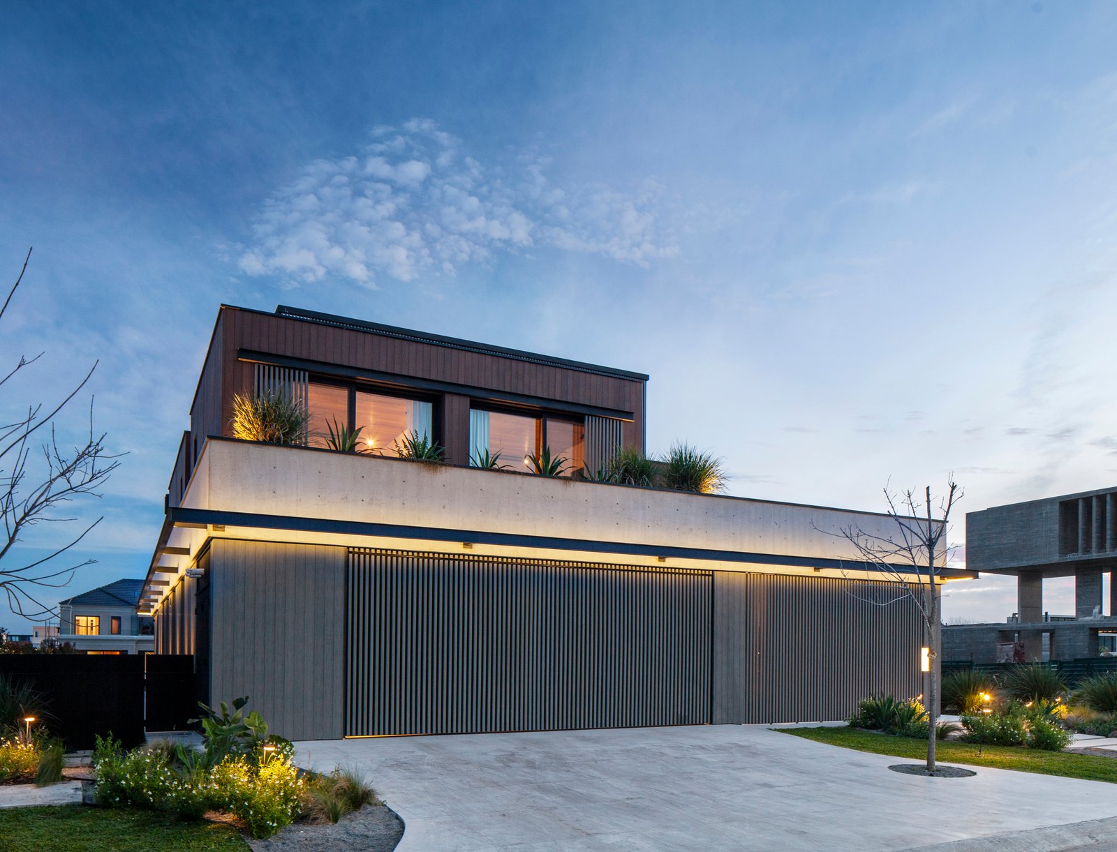 fachada de casa moderna con luces cálidas y detalles de madera — proyecto Obra Warehouse, por lifecycle, en Nordelta
