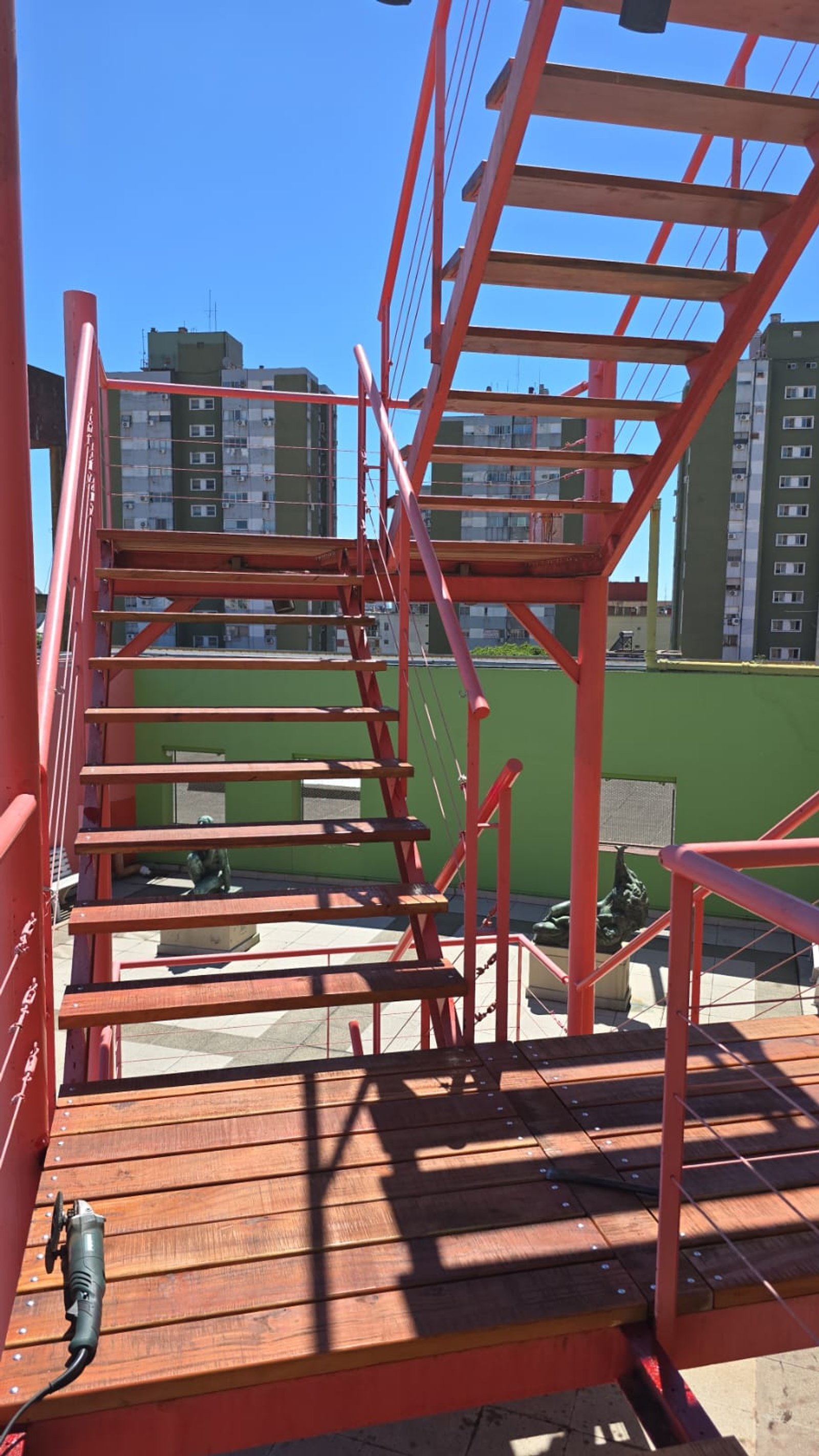Escada metálica vermelha sobre deck de madeira — projeto Museo Benito Quinquela Martin, por ASV Muebles y Maderas, em Av. Don Pedro de Mendoza 1835