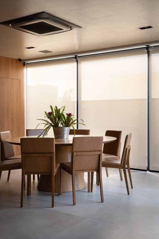 Comedor minimalista con mesa redonda y sillas de madera frente a ventanal — proyecto Casa Lago Sul, por Daniel Santo