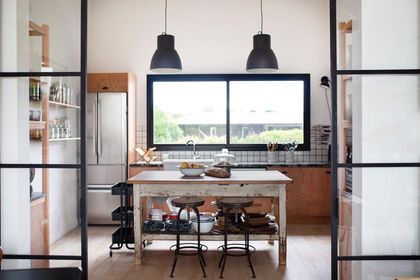 Cocina moderna con isla de madera, ventanal amplio y lámparas colgantes negras — proyecto JI 103, por Estudio Diez Muzzio