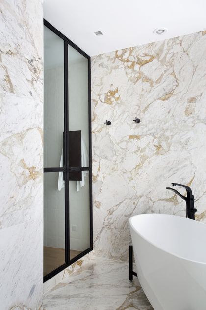 Baño moderno con mármol blanco, bañera blanca y mamparas negras — proyecto BM House, por Studio Ro-ca
