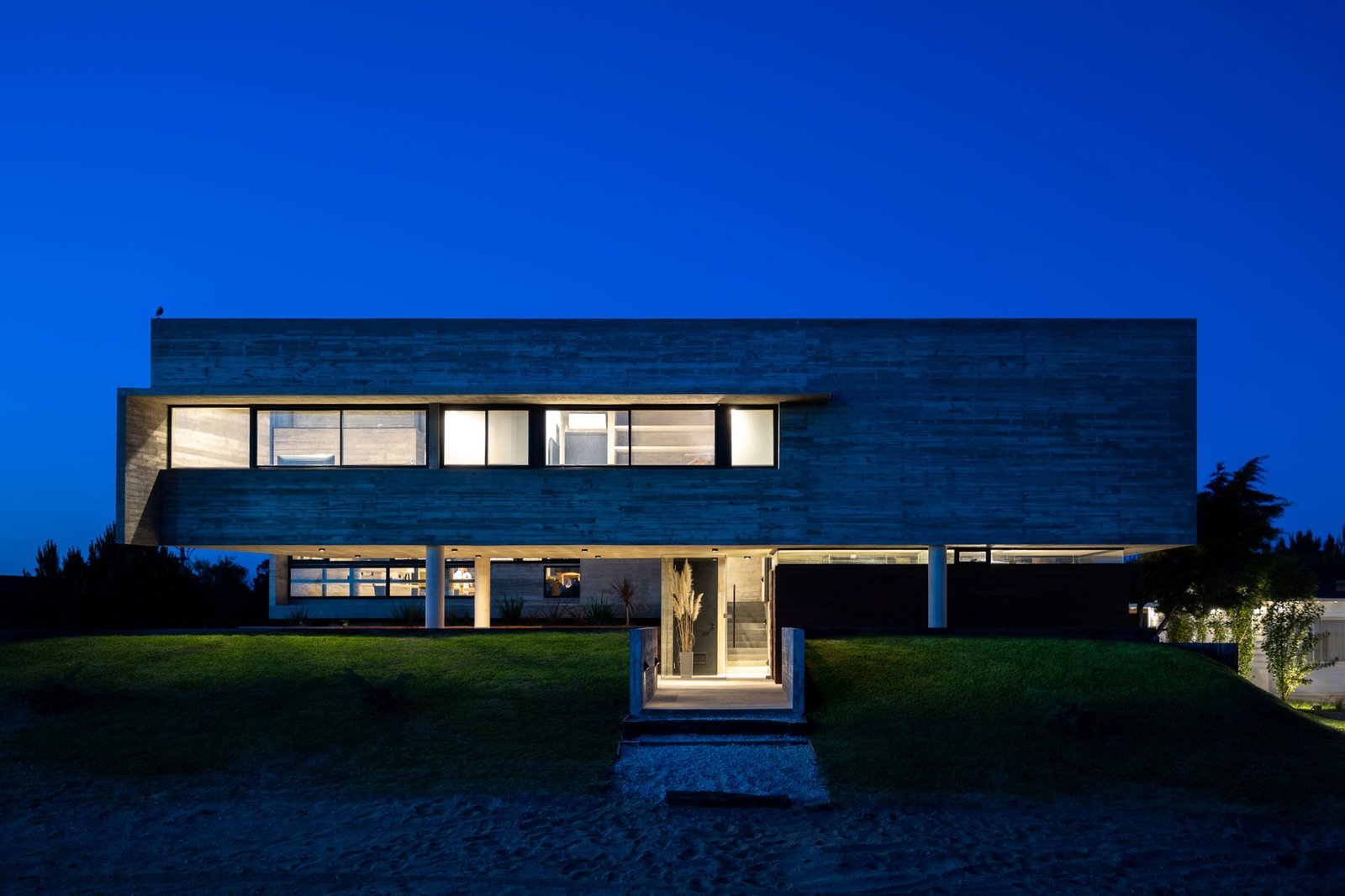 Fachada moderna de hormigón con amplios ventanales, vista nocturna rural — proyecto Casa La Marina, por Besonías Almeida arquitectos, en X6VF+67