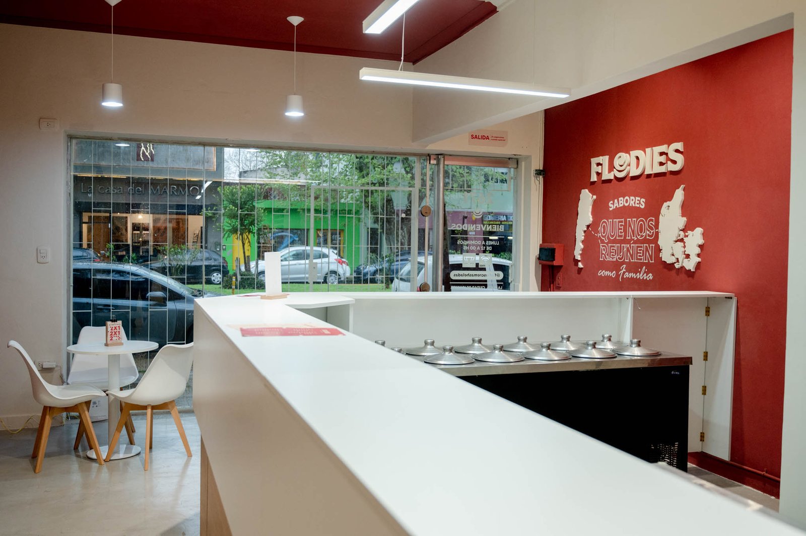 Local comercial moderno con mostrador blanco y pared roja — proyecto Flodies Cremas heladas, por Ailén Lucero Arquitectura, en La Plata