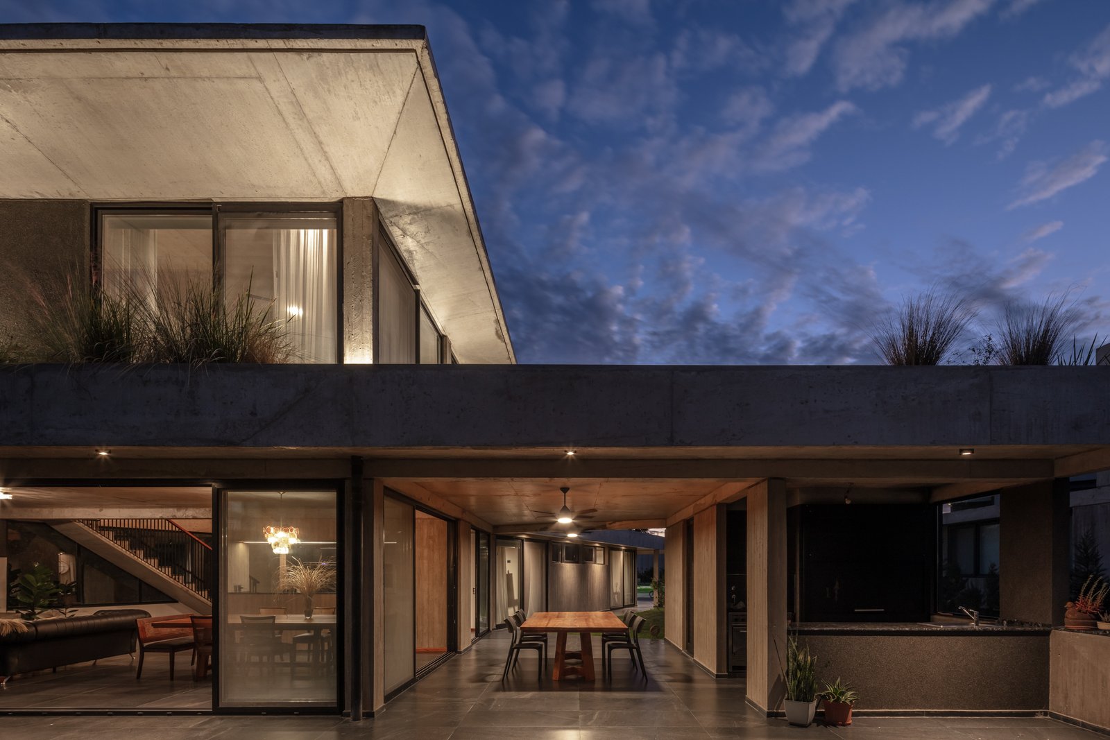 Residência brutalista com concreto aparente e amplas janelas ao entardecer — projeto La Martona UF280, por BARBALACO ARQUITECTOS, em Provincia de Buenos Aires