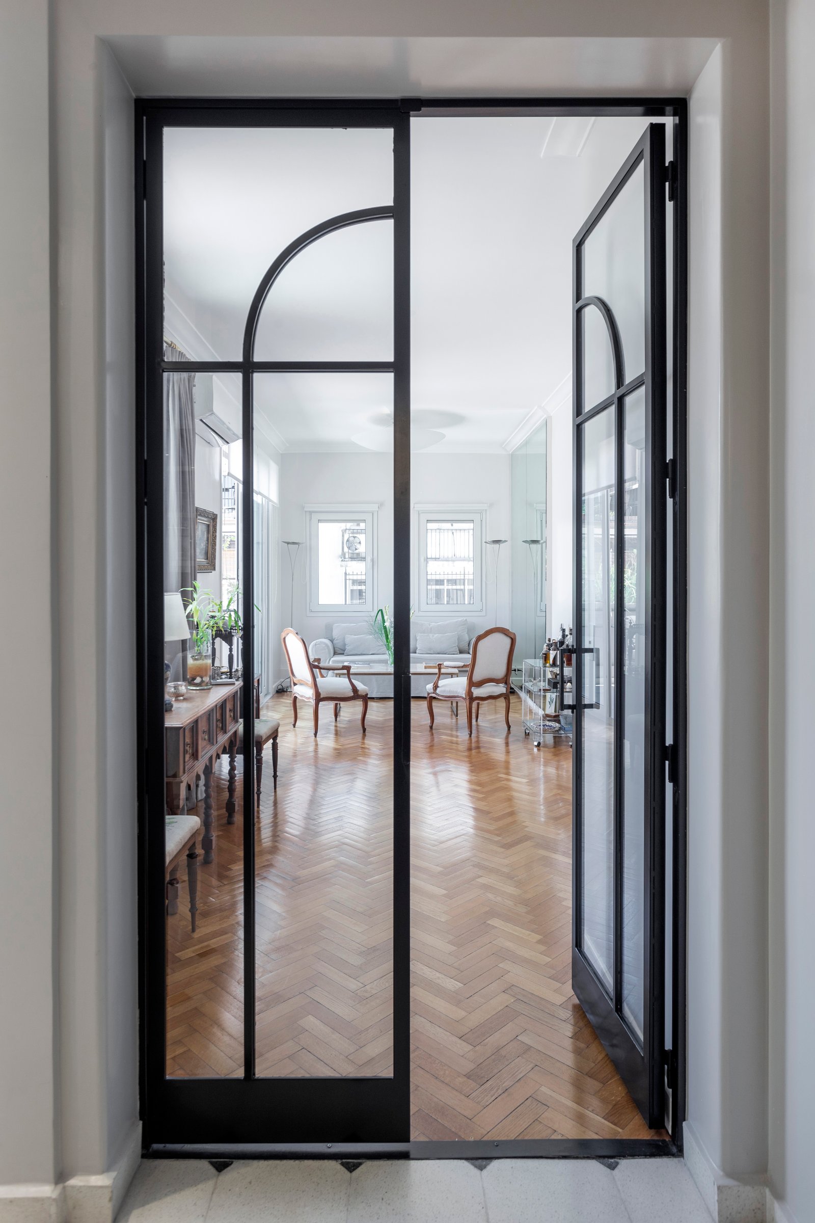 Living con puertas vidriadas y pisos de madera a espiga — proyecto Ayacucho, por JT ARQUITECTURA, en Buenos Aires