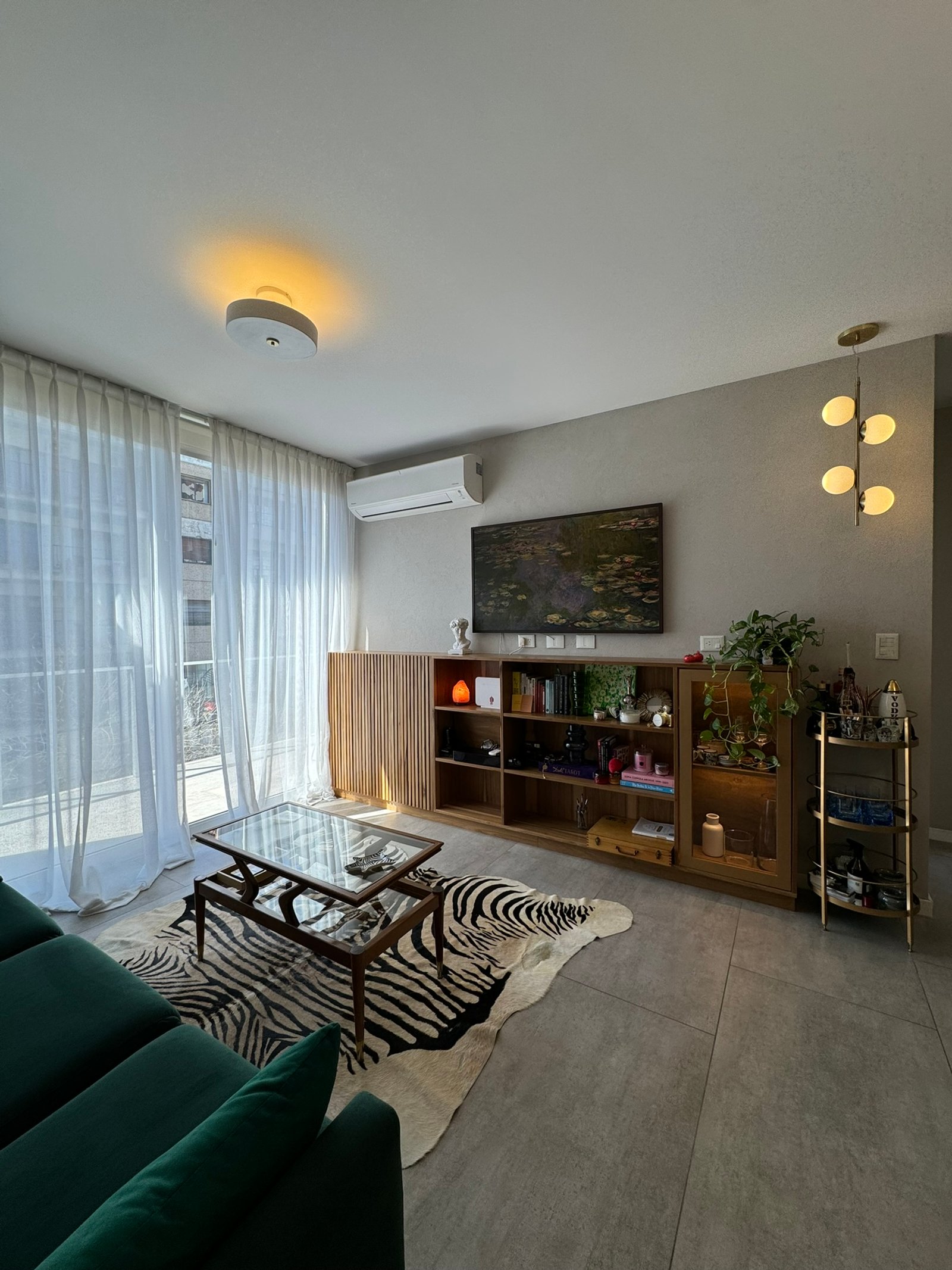 Living moderno con sofá verde, alfombra cebra y estanterías de madera — proyecto Freire, por MDBK Arquitectura, en Belgrano