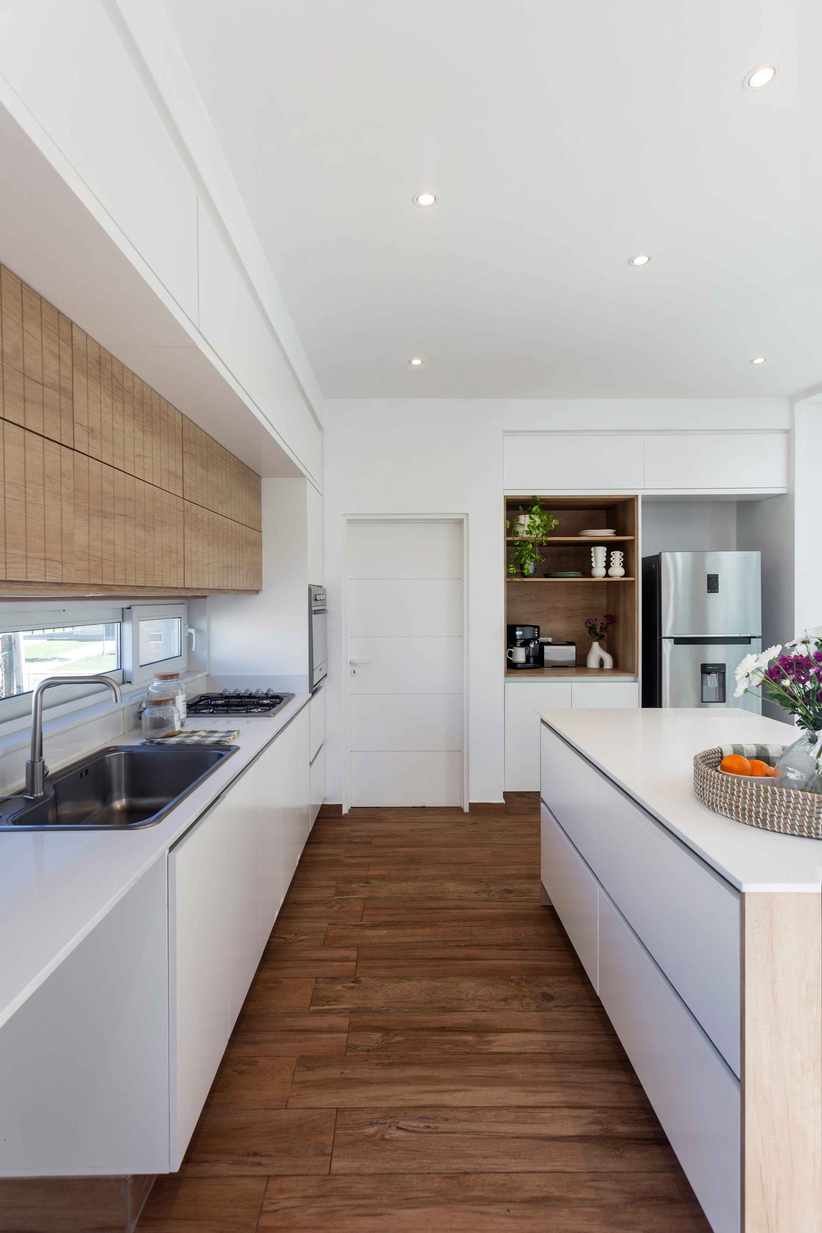 Cocina moderna con isla, muebles blancos y detalles en madera — proyecto SANTA INÉS I, por Estudio Stepa, en Canning