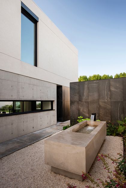 Fachada moderna con fuente de concreto y muro de piedra — proyecto CASA SD28, por GMARQ, en Buenos Aires