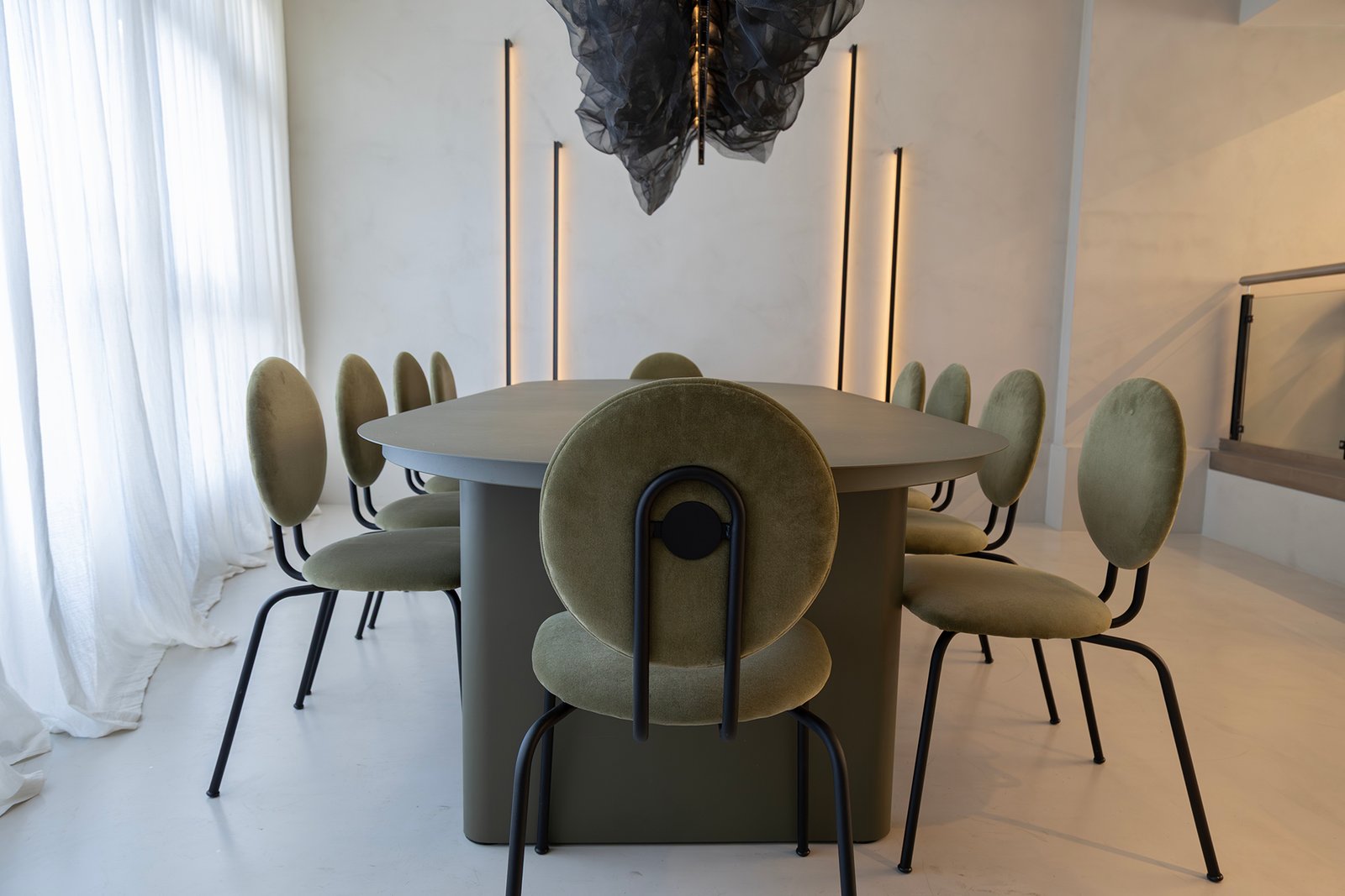 Comedor moderno con mesa ovalada, sillas curvas verdes y lámpara colgante dramática — proyecto HATSU Núñez - MZV Arquitectura, por Gaby Alfonso, en Buenos Aires