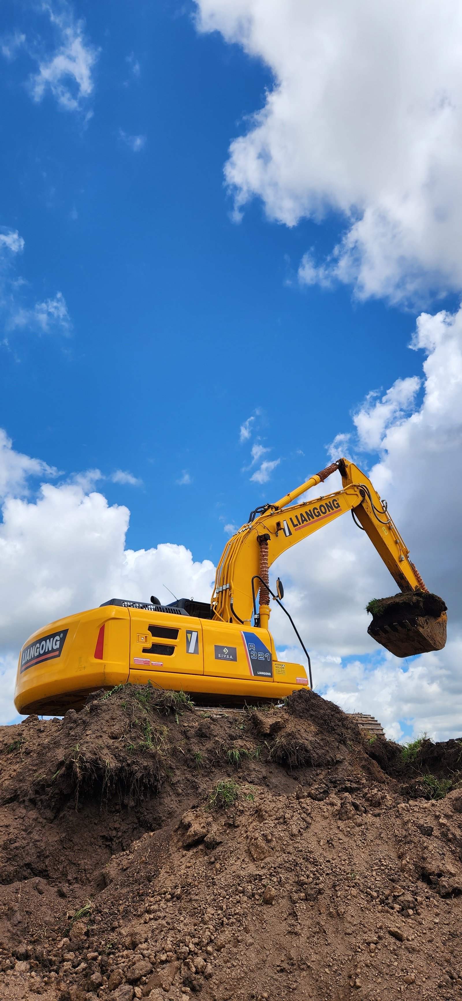 Excavadora amarilla en obra sobre montículo de tierra con cielo azul — proyecto Central Park - Terralagos, por Estudio Rifahi, en Canning