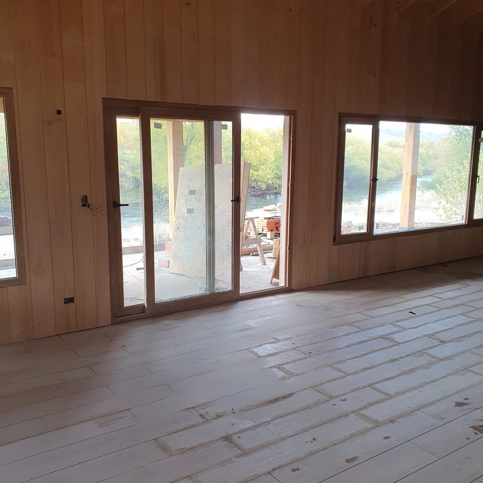 Interior de obra con madera clara y grandes ventanales — proyecto Vivienda a orillas del Río Quilquihue, por TROKEN, en Neuquén