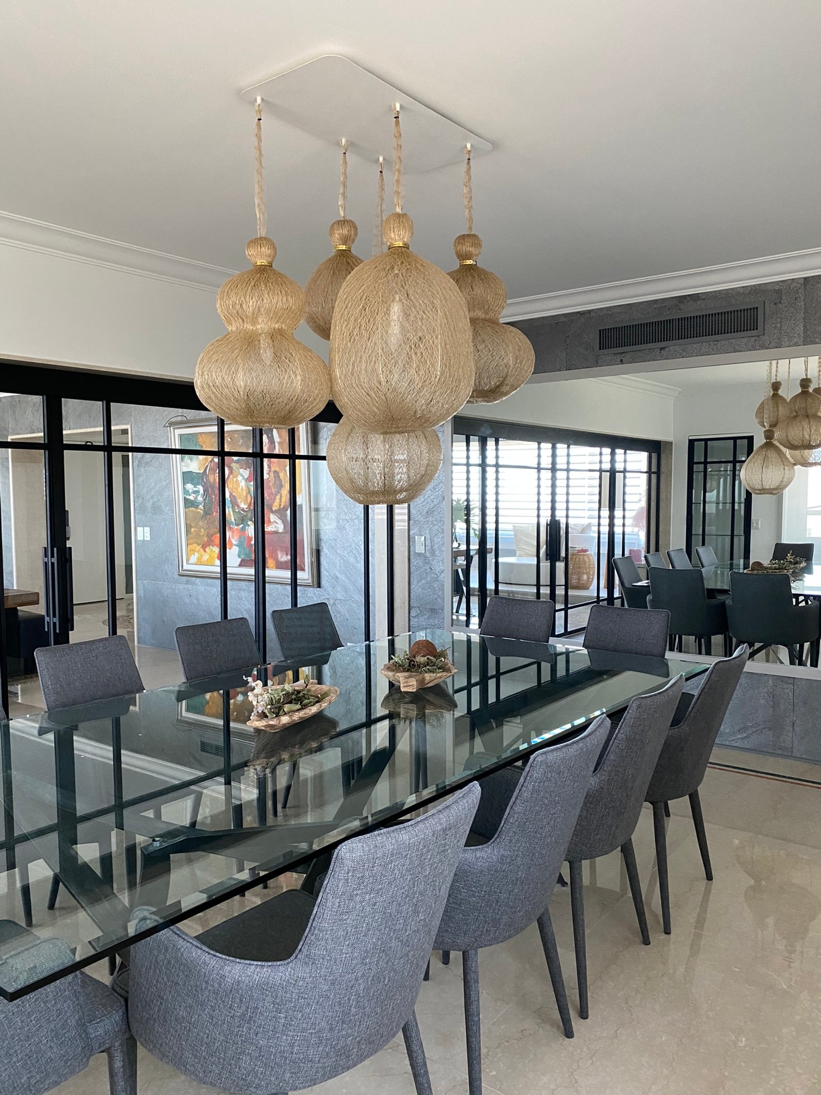 Sala de jantar moderna com mesa de vidro, cadeiras cinzas e luminárias de rattan — projeto Libertador I, por MDBK Arquitectura, em Palermo