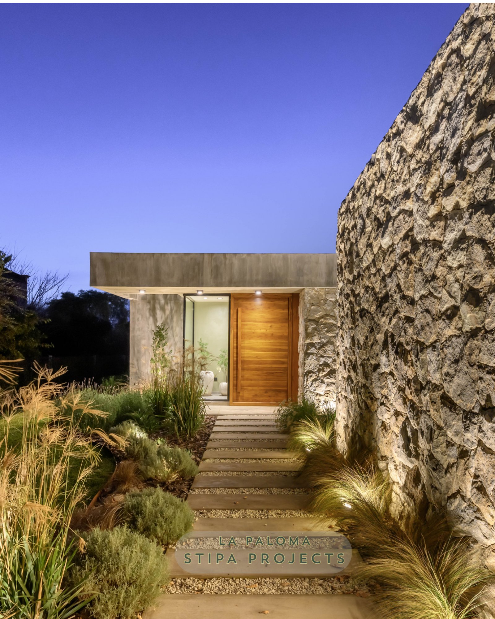 Entrada moderna con muro de piedra y vegetación exuberante al anochecer — proyecto La Paloma :: Villa Allende - Córdoba :: Paisajismo Residencial :: STIPA Arte Nat, por STIPA Arte 