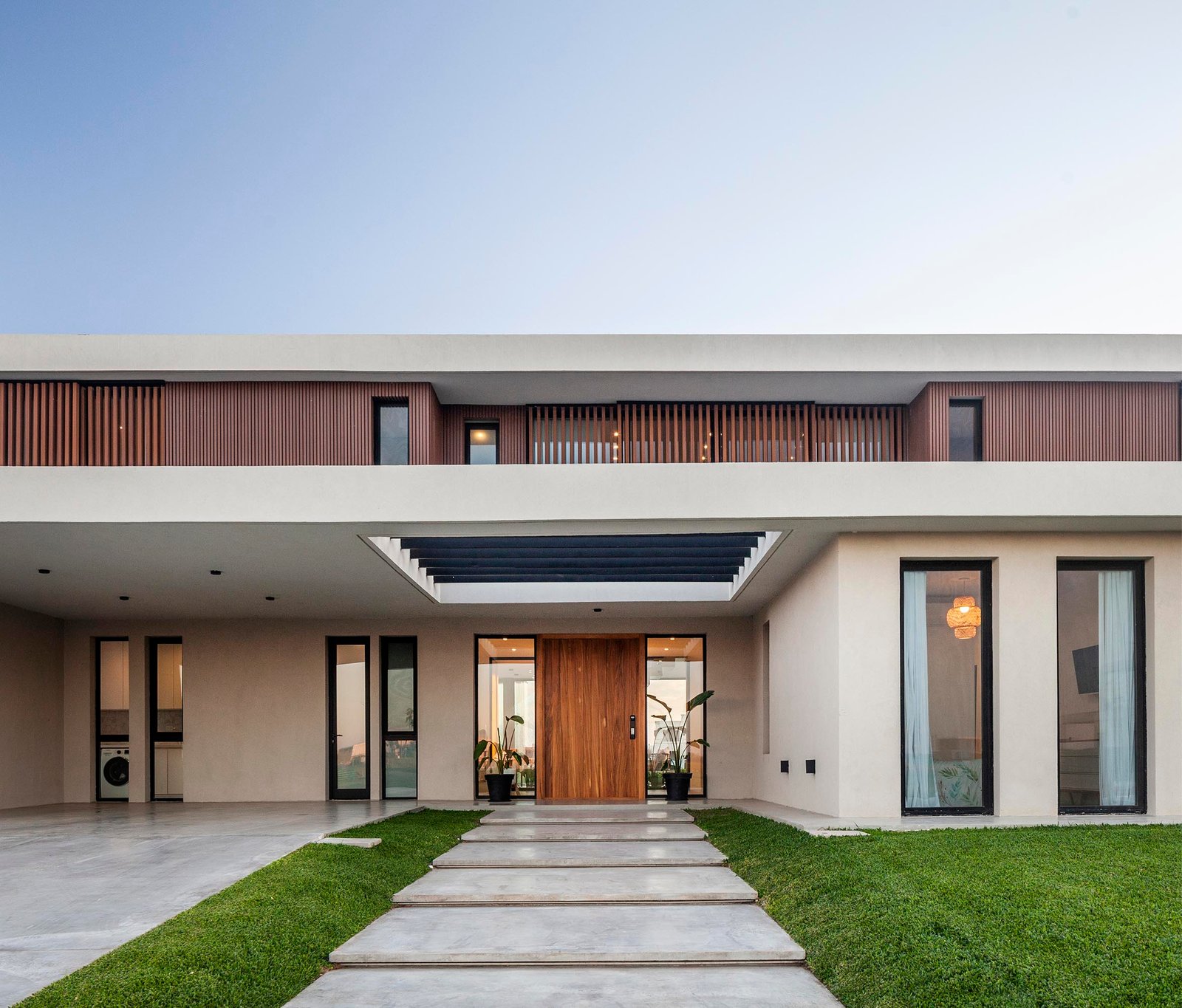 Fachada moderna con puerta pivotante de madera y revestimiento de hormigón — proyecto CASA C313, por A'PRIMA - Arquitectura Sustentable, en Provincia de Buenos Aires