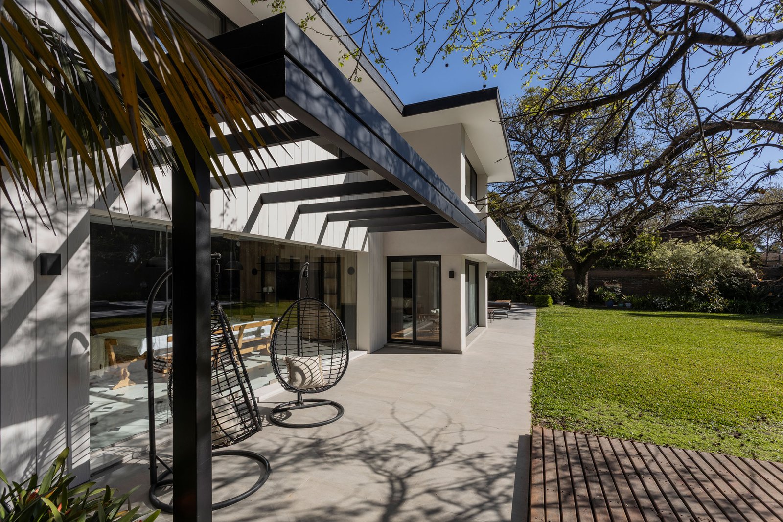 Fachada moderna con patio de hormigón y sillas colgantes de mimbre — proyecto REFORMA DG, por Rastro Estudio, en Punta Chica