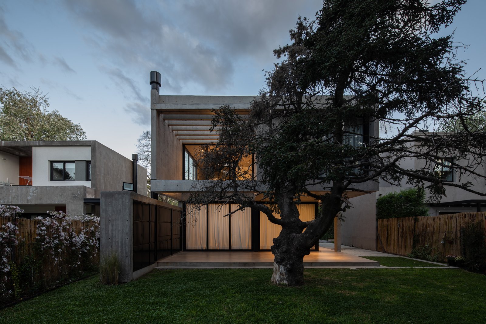 Fachada moderna con hormigón y madera, rodeada de árboles — proyecto Casa Emilia, por Grupo CRBN, en Parque Leloir