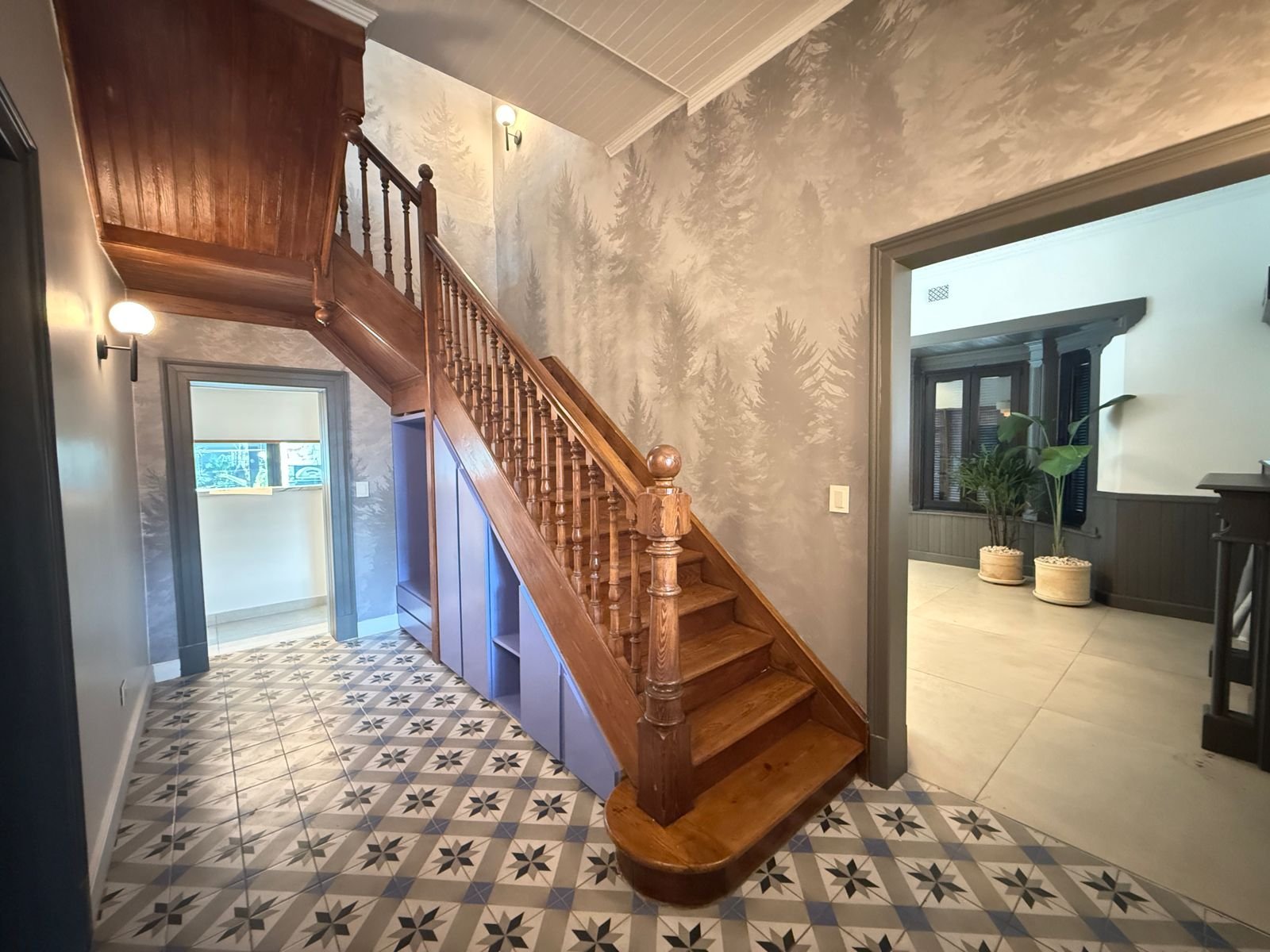 Corredor com escada de madeira ornamentada e papel de parede de árvores — projeto vivienda unifamiliar, por Alchemyst artisan studio, em Lomas de Zamora