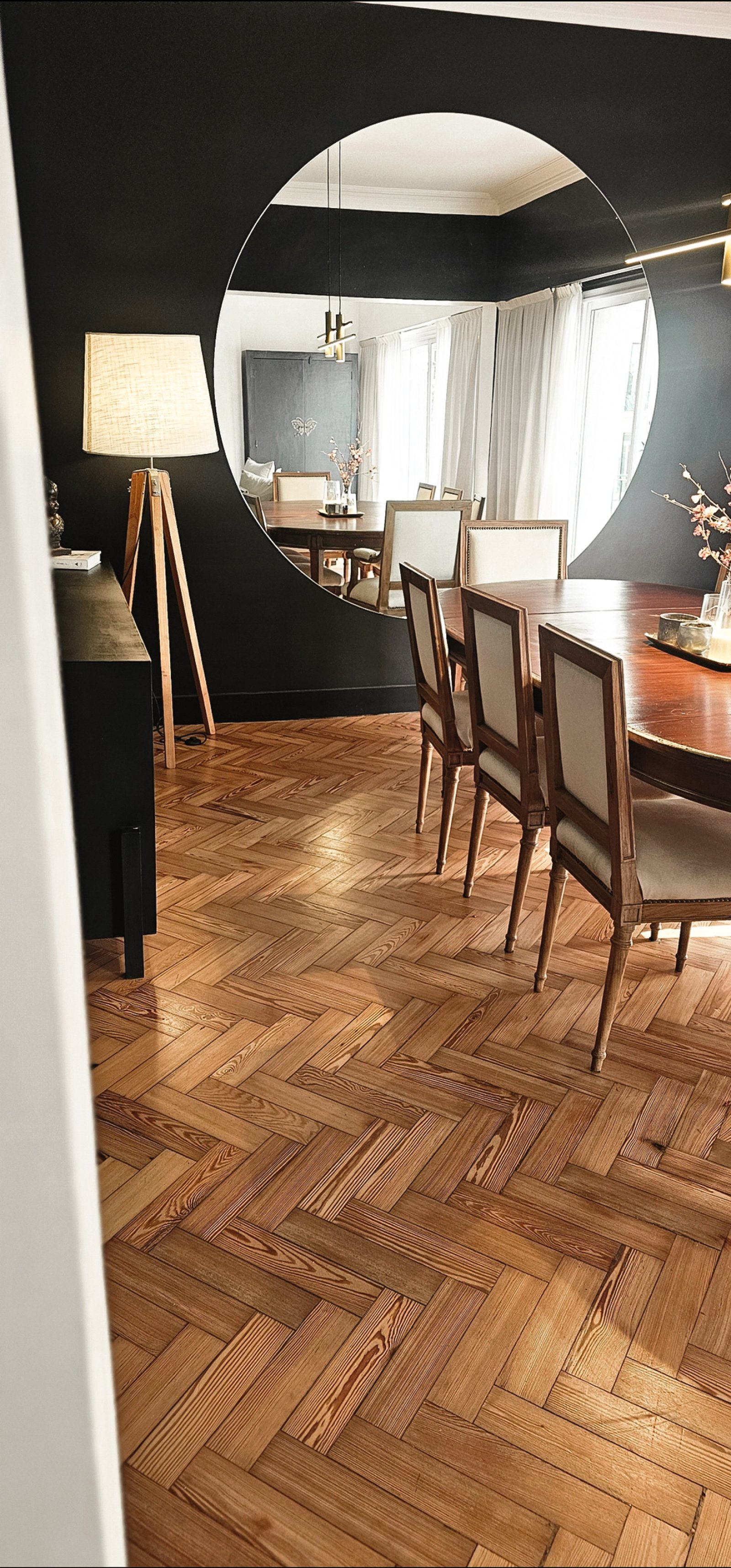 Sala de jantar moderna com espelho curvo, piso de madeira espinha de peixe e paredes escuras — projeto Cabello, por Claraboia, em Palermo