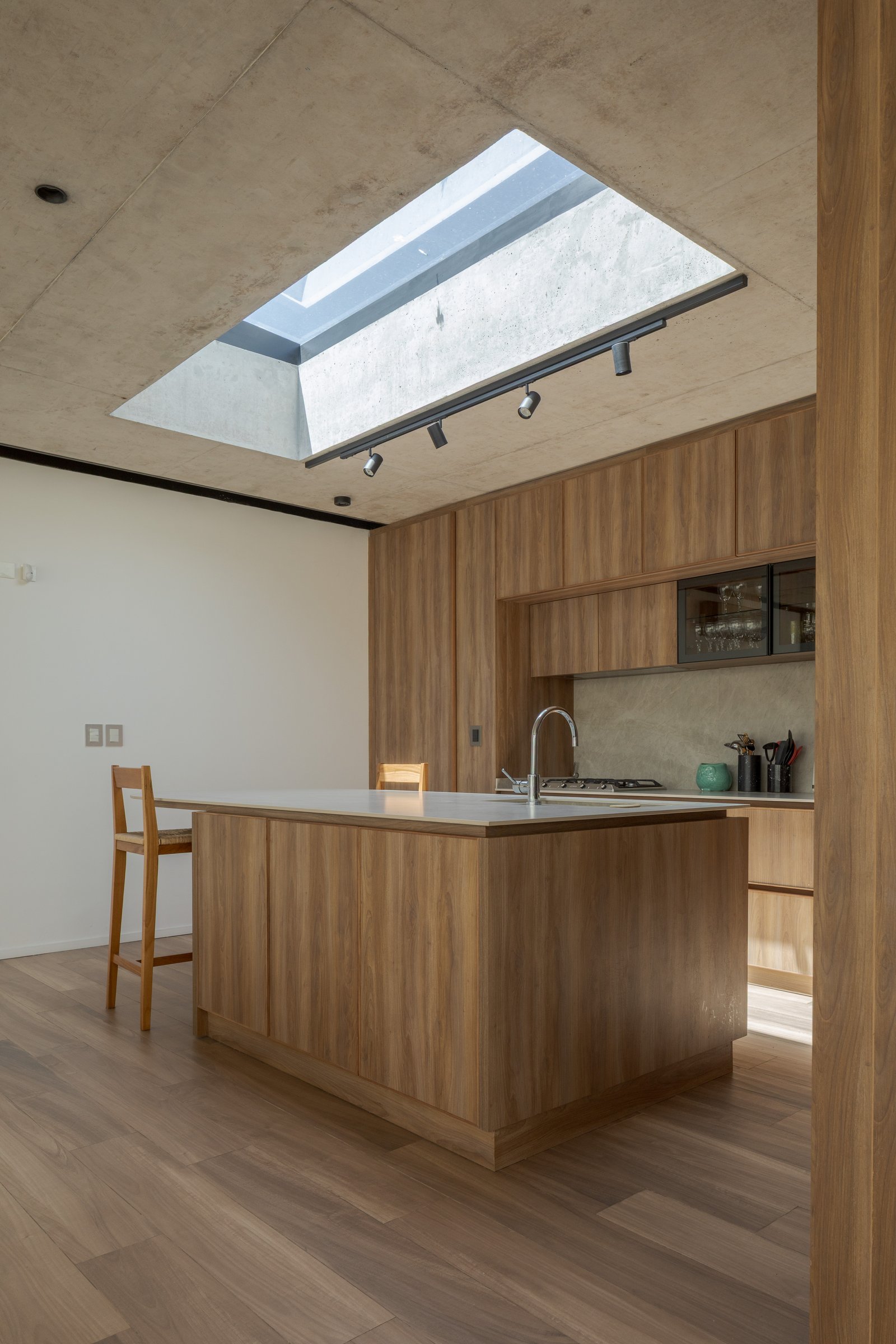 Cocina moderna con isla central y gran claraboya de hormigón — proyecto Casa PLANALTO, por Grupo CRBN, en Av. Pres. Perón 10298