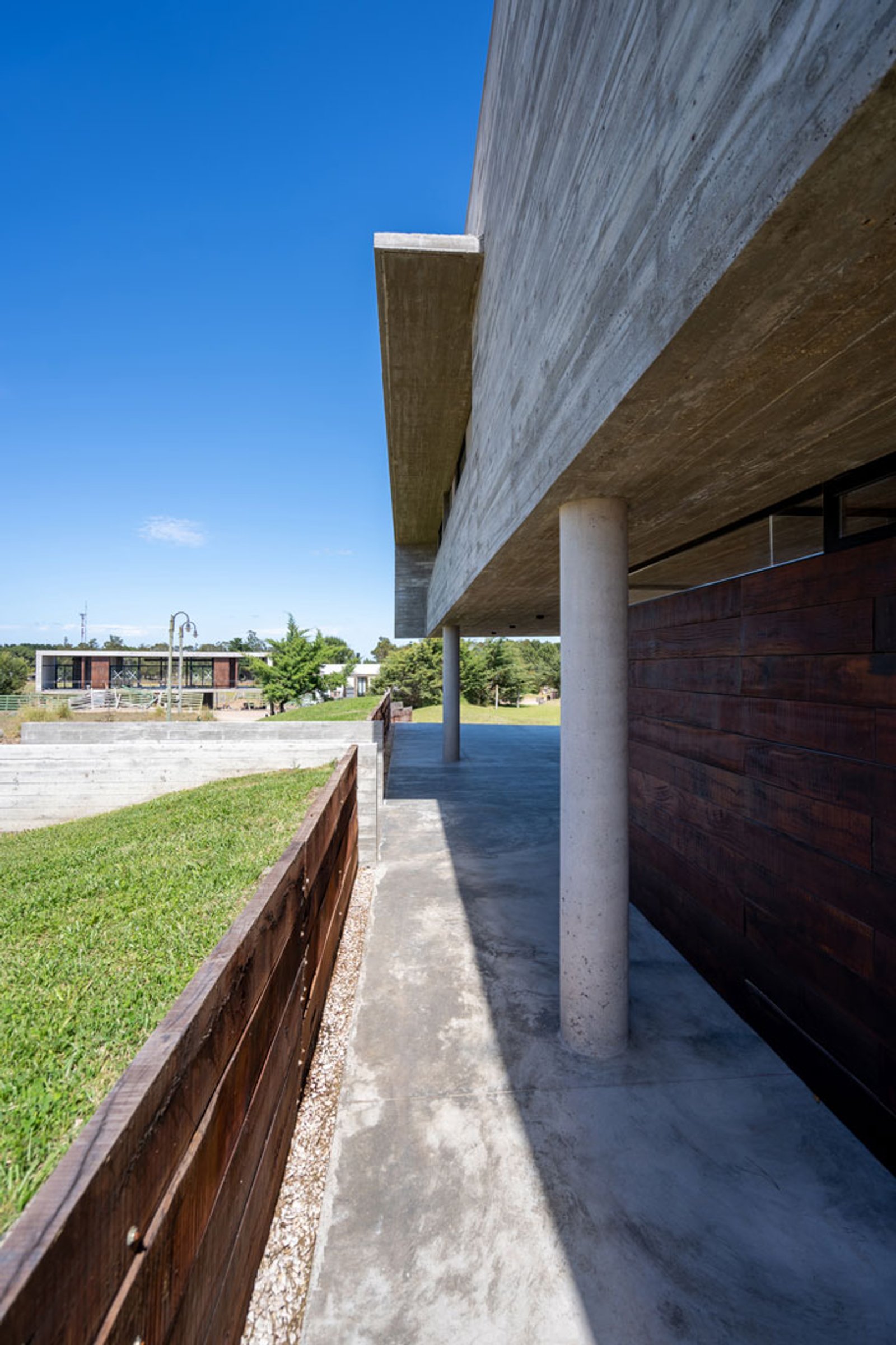 Fachada moderna de hormigón visto y madera con cielo azul — proyecto Casa La Marina, por Besonías Almeida arquitectos, en X6VF+67